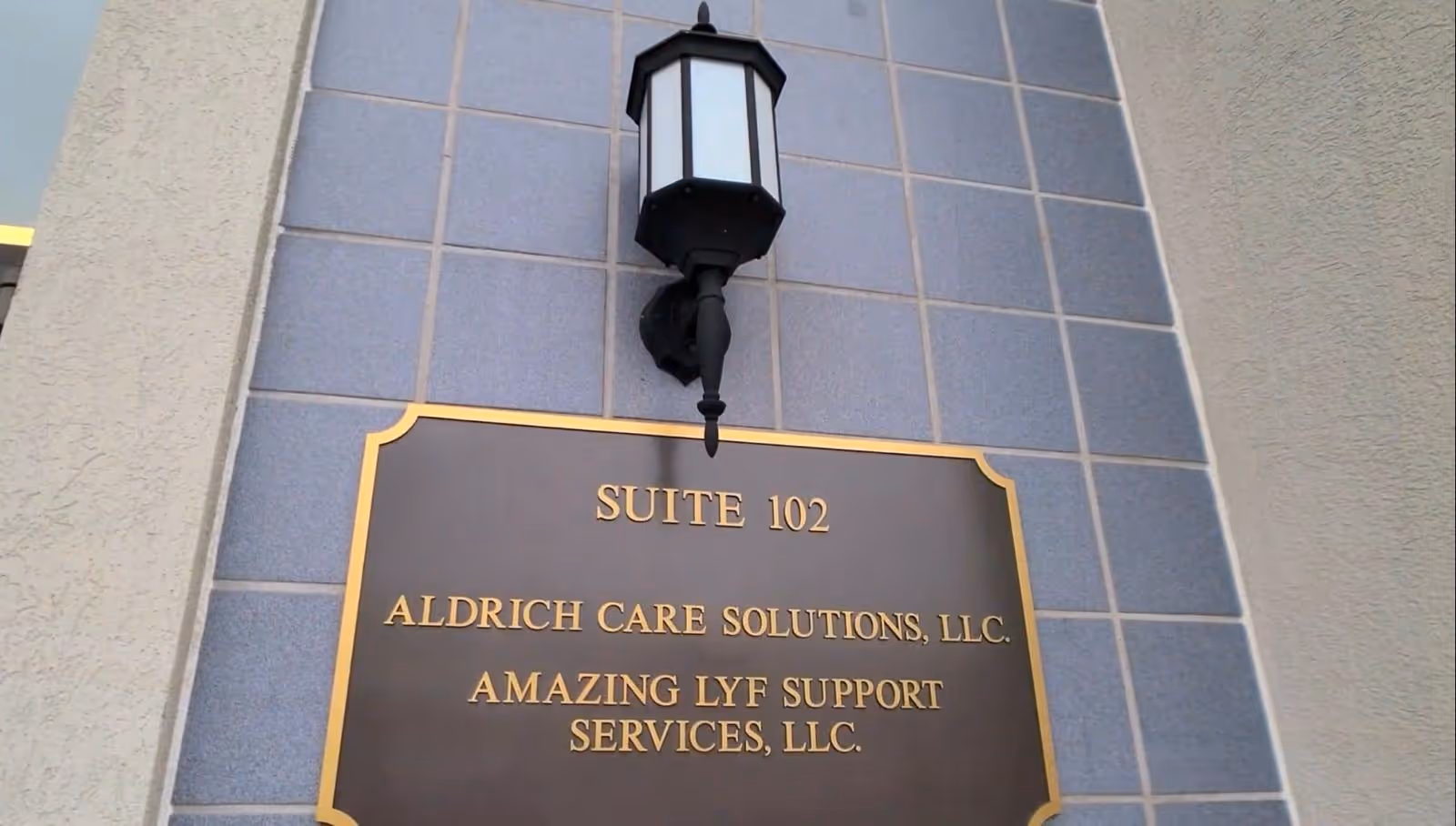 Exterior wall sign reading Suite 102 and Aldrich Care Solutions, LLC beneath a lantern.