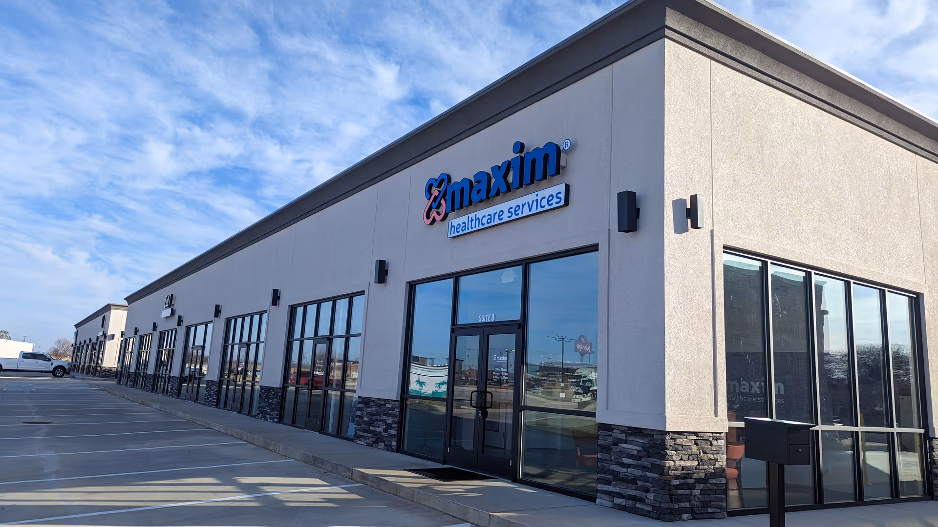 Exterior view of Maxim Healthcare Services office building with glass storefronts and a parking lot.