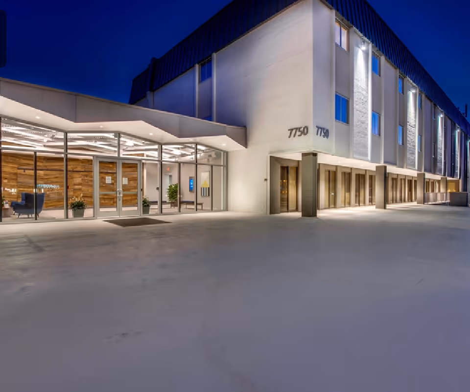 Night exterior of a modern senior living facility with glass entrance and lit lobby.