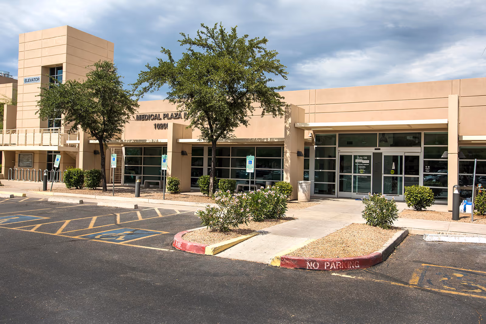 Exterior view of a beige medical plaza with glass entrance doors and parking.