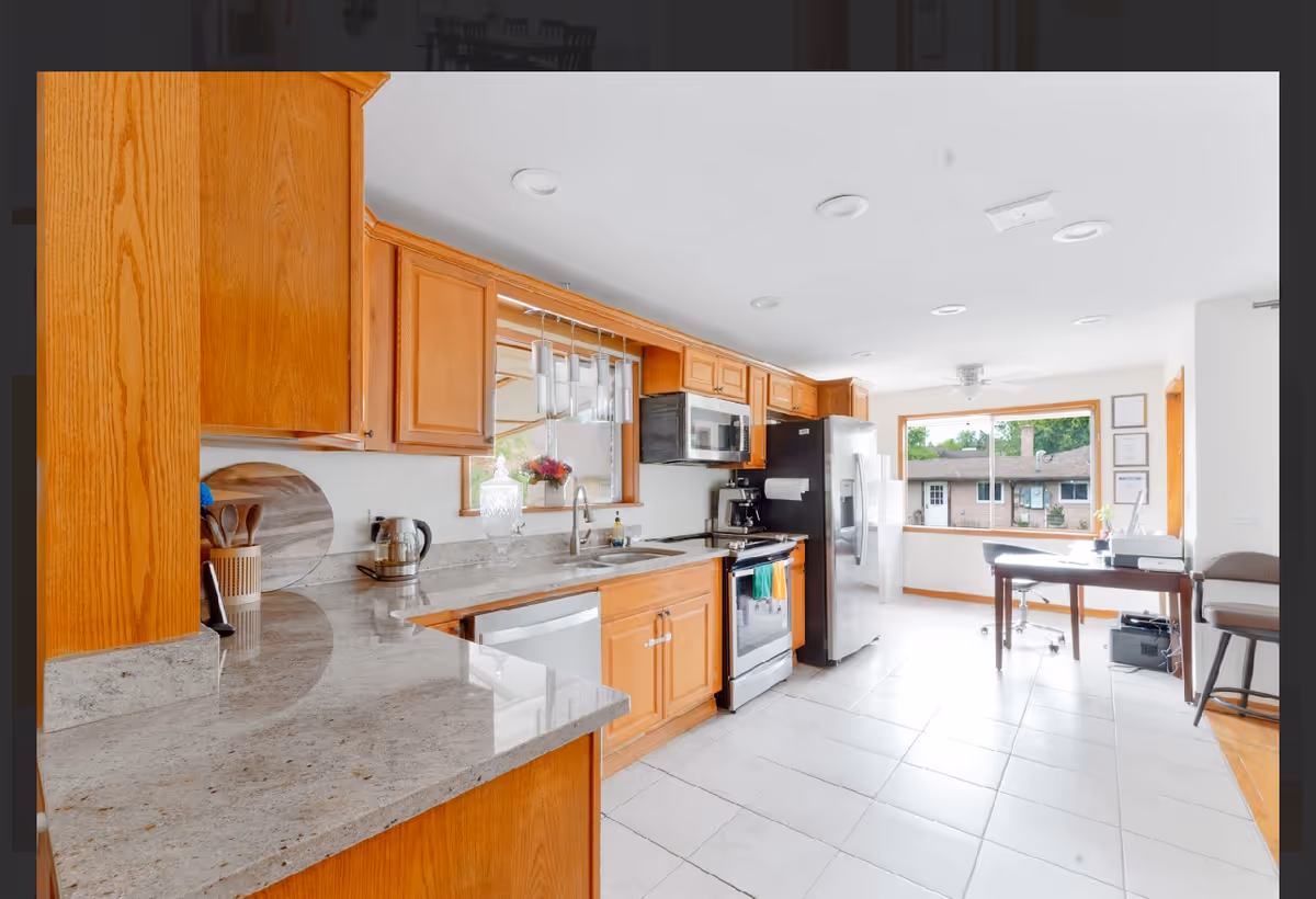Bright kitchen with wooden cabinets, stainless appliances, and a desk by a large window.