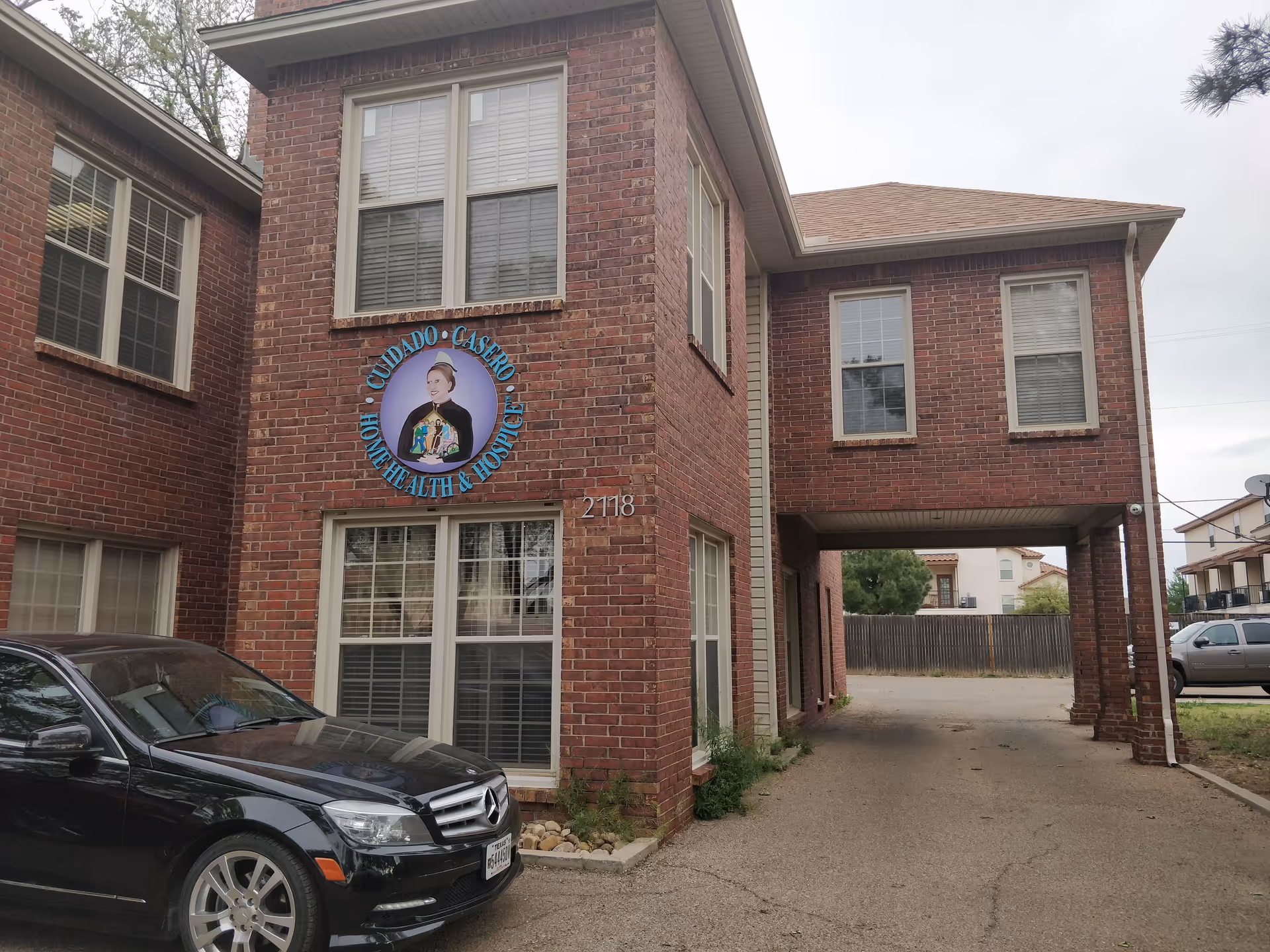 Brick two-story senior care building with circular sign, archway driveway, parked black car.