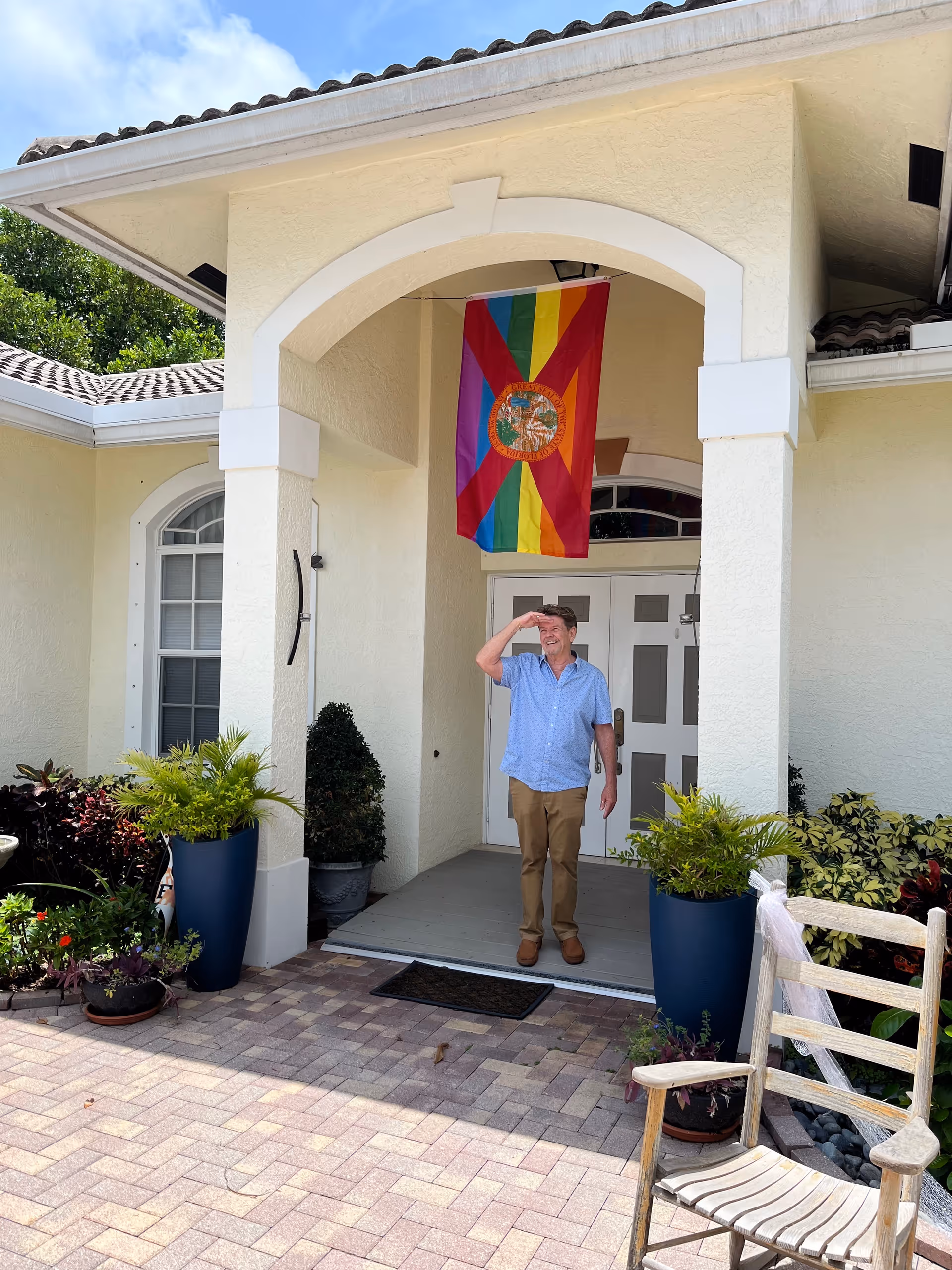 A man stands on a porch at Candy Cohn senior living entrance beneath a colorful flag.