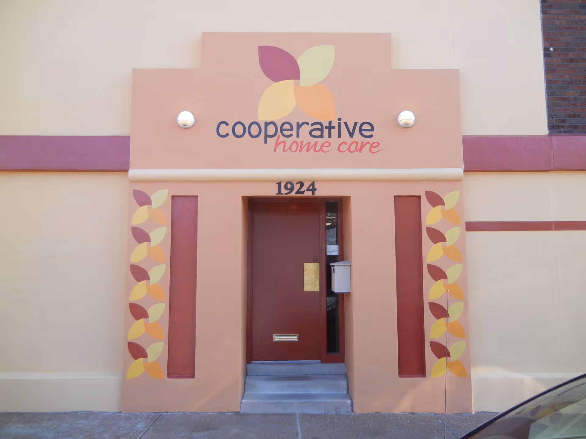 Front entrance of Cooperative Home Care building with peach facade and decorative leaf motifs.