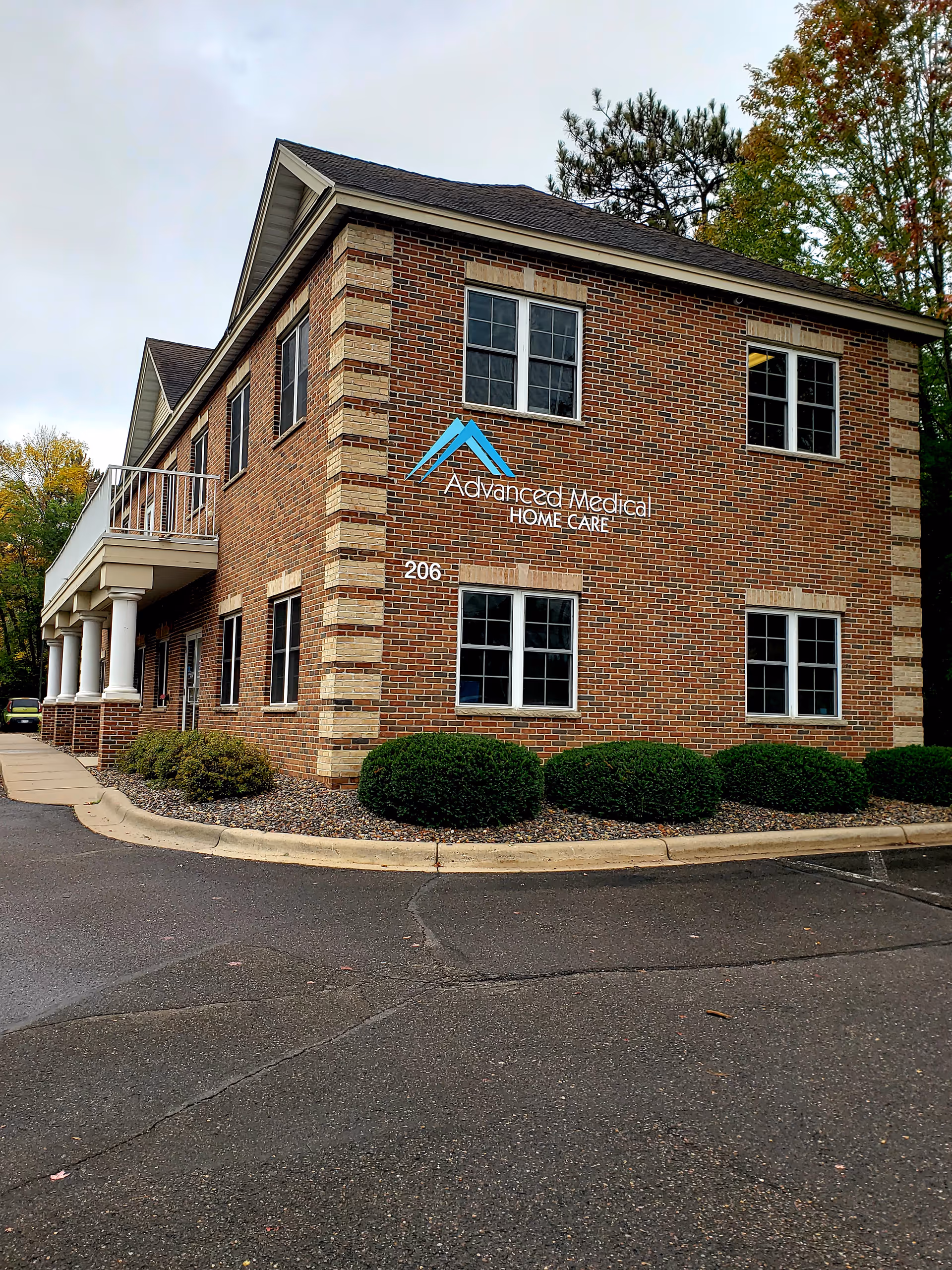 Brick two-story building with 'Advanced Medical Home Care' sign and manicured shrubs in front