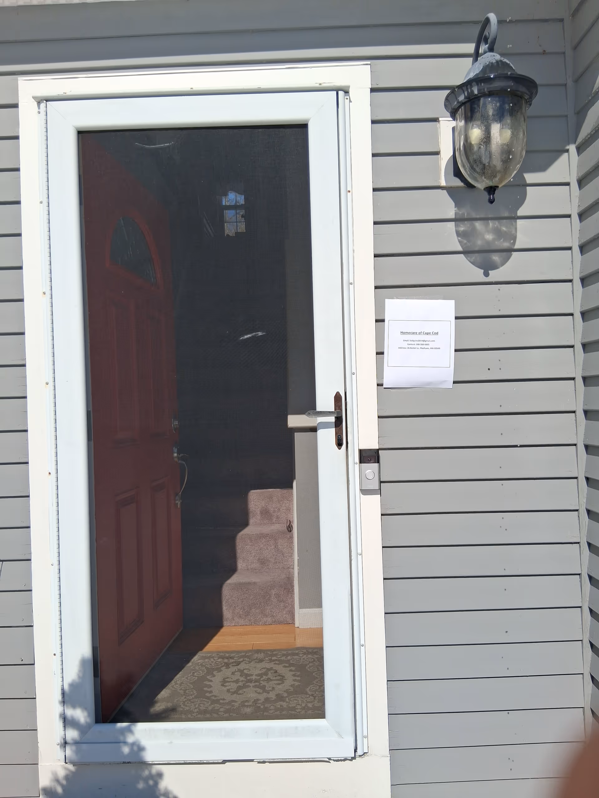 Open front door of a gray exterior building with a lantern-style light fixture.