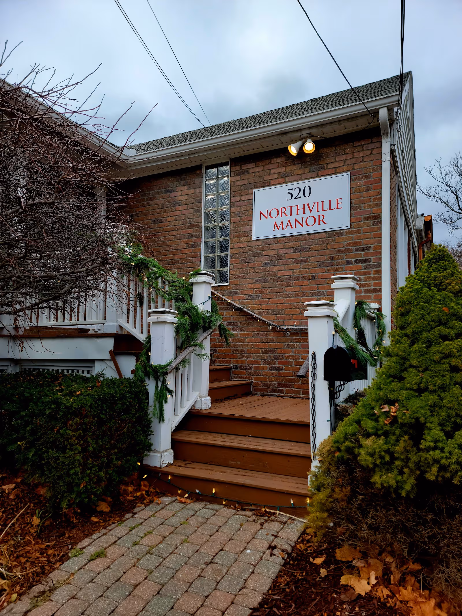 Exterior of a brick senior living building with steps, white railings, garland, and a sign.
