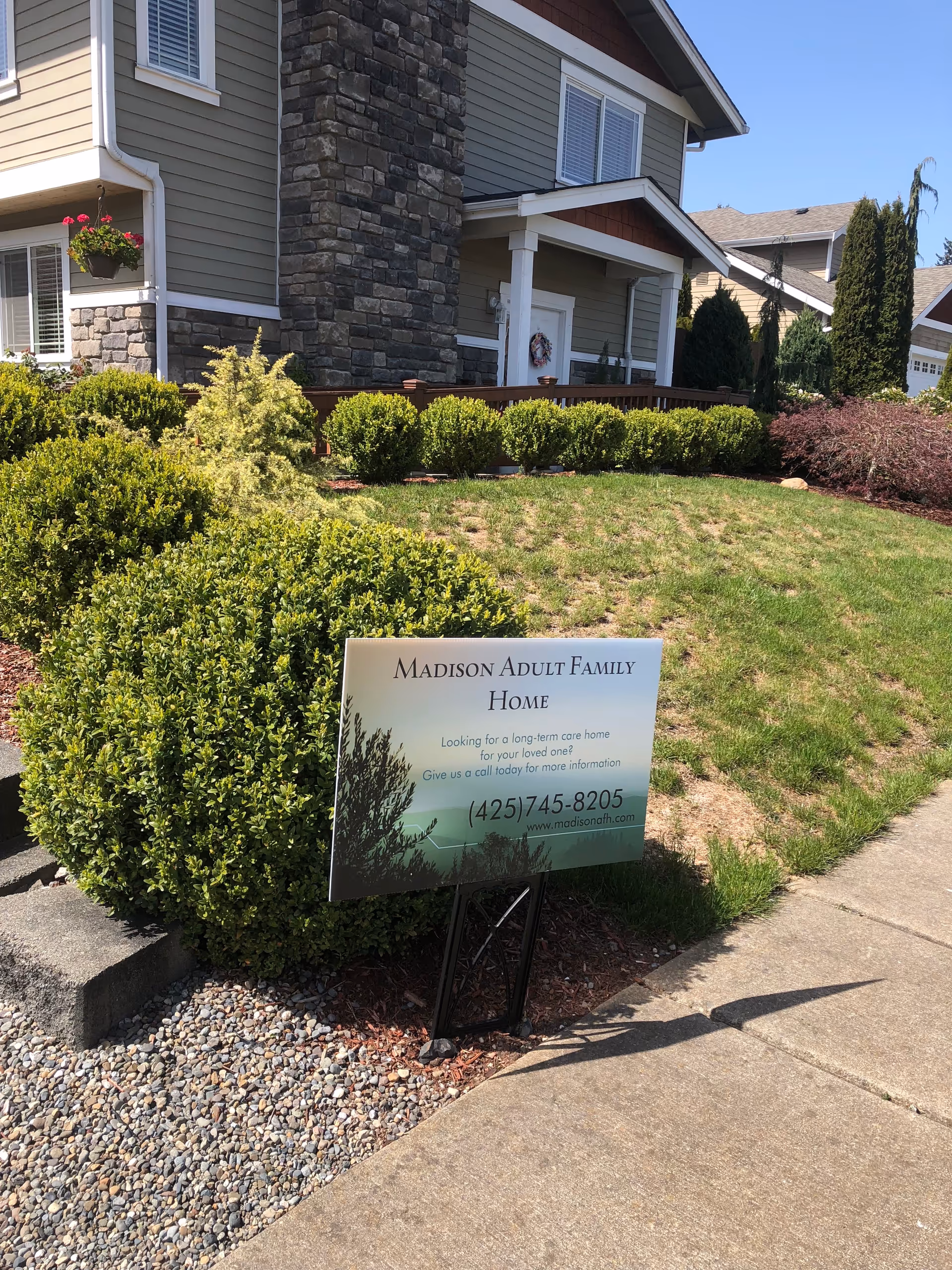 Front exterior of Madison Adult Family Home with landscaped lawn and a sign near walkway