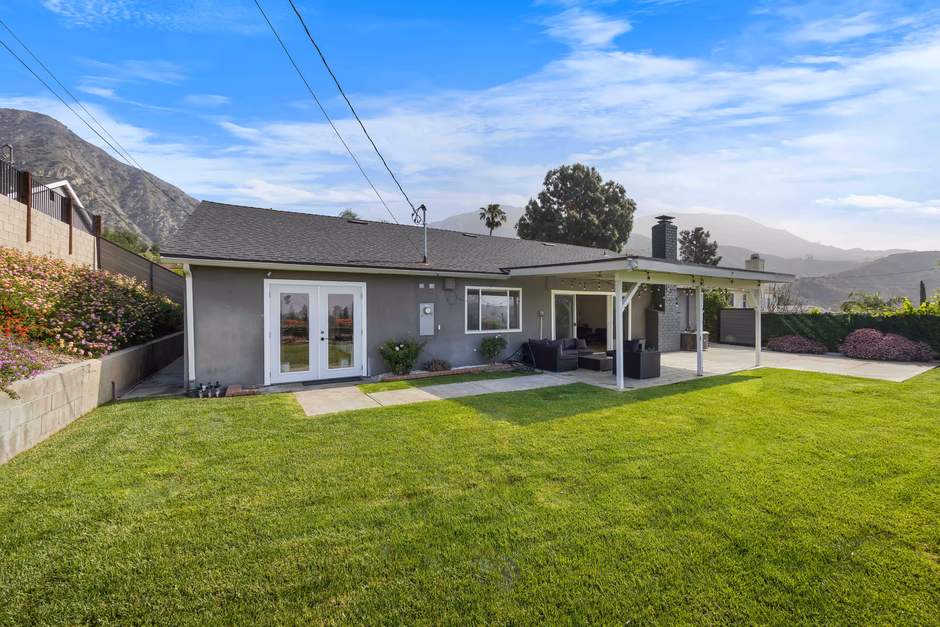 Single-story house with a large green lawn, covered patio, and outdoor seating.