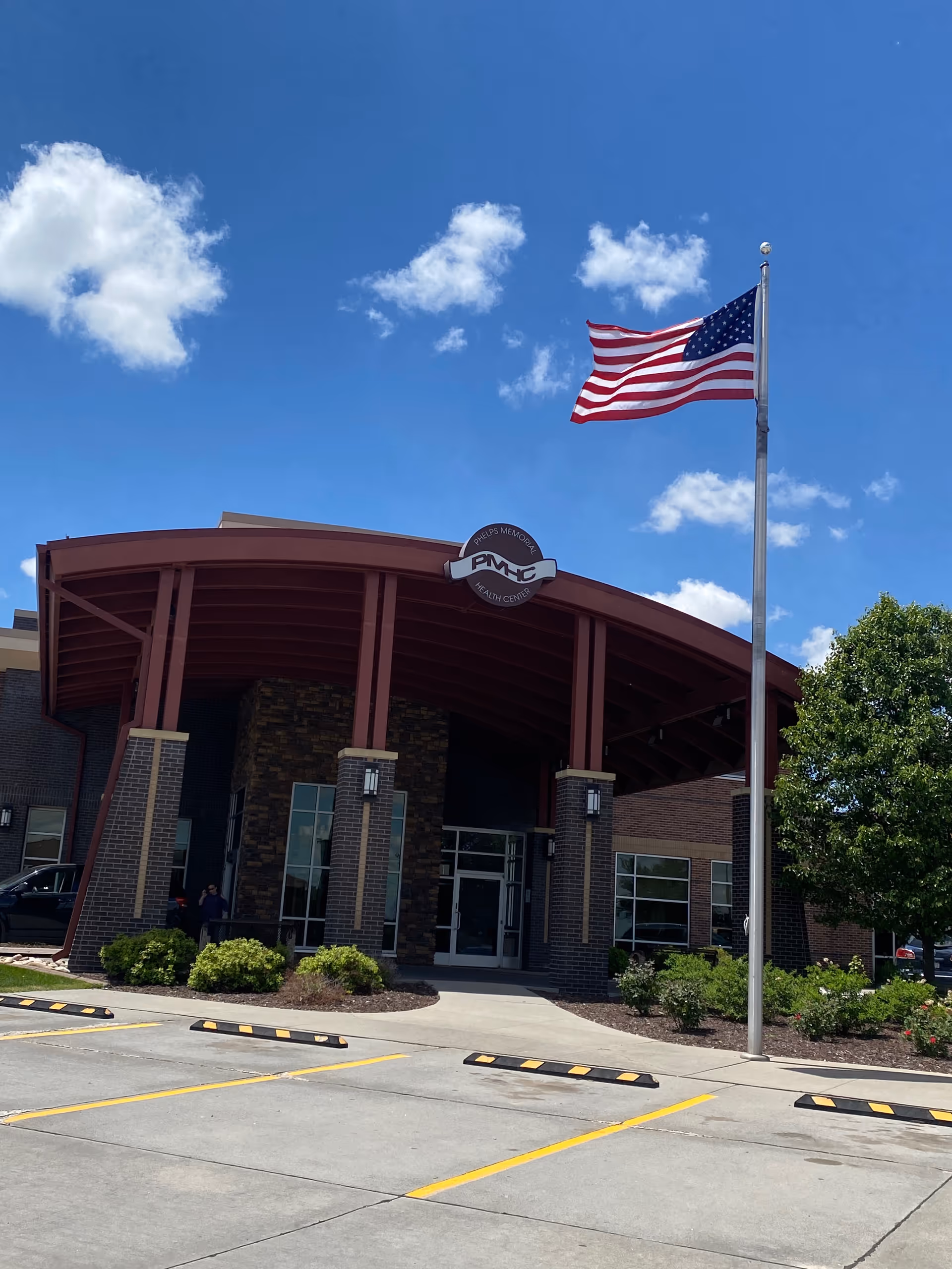 American flag beside the curved entrance of Phelps Memorial Health Center building front.