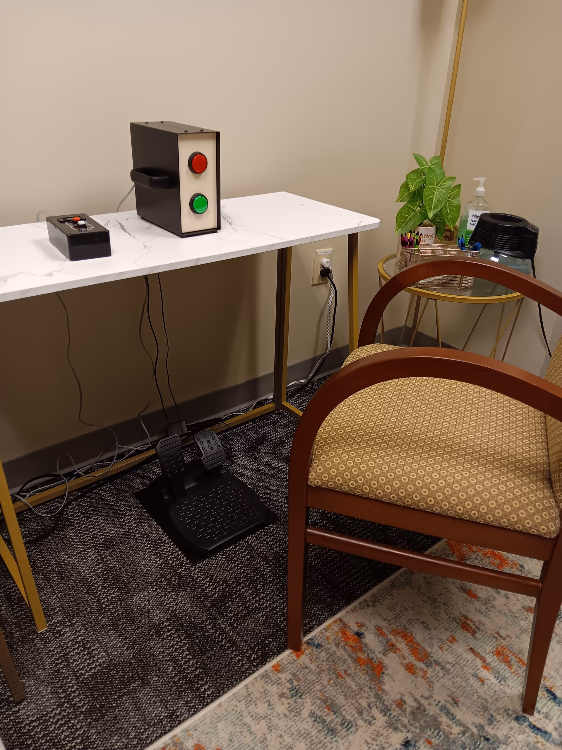 Interior corner featuring marble desk with foot pedal, chair, plant, and hand sanitizer.