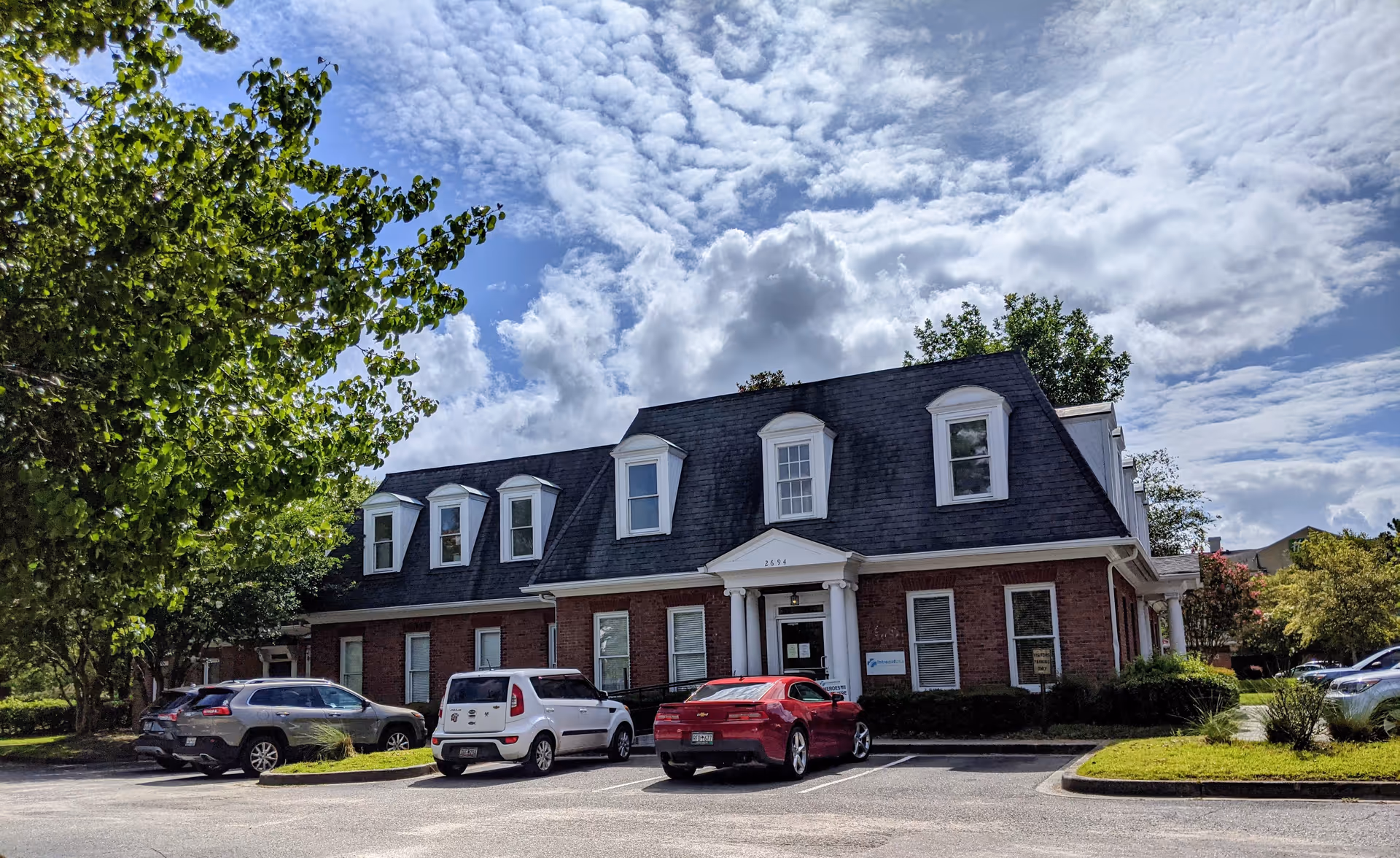 Brick senior living facility with dormer windows and a parking lot in front.