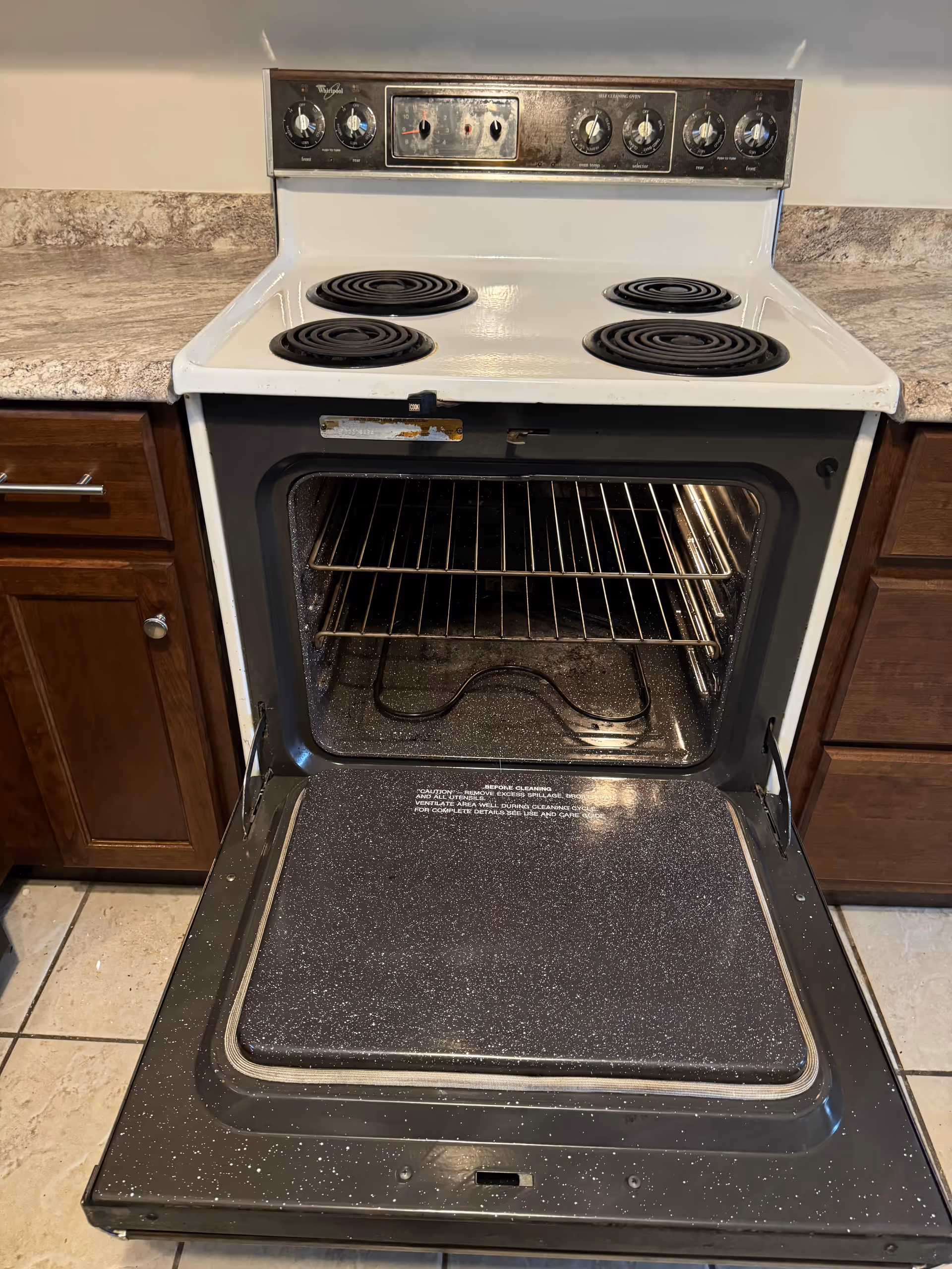 Open electric oven with four coil burners in a kitchen with wood cabinets.