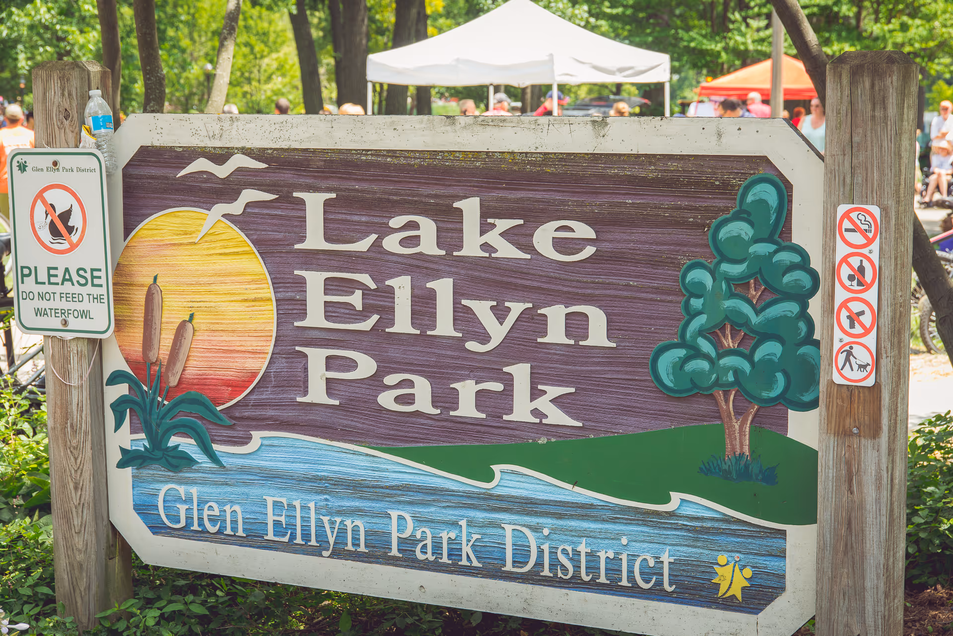Park sign reading Lake Ellyn Park with people visible in the background.