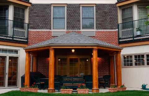Brick senior living building exterior with a covered patio, wooden columns, and outdoor seating.