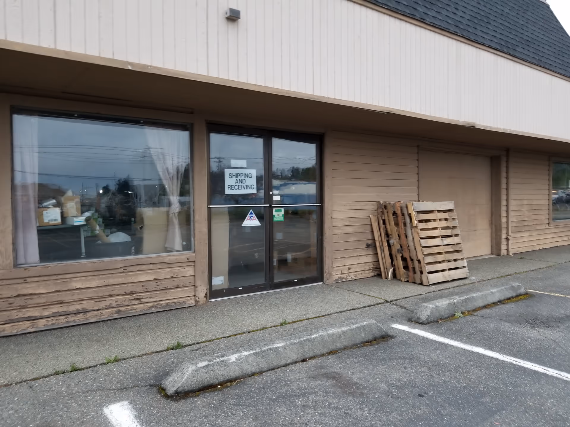 Exterior of a brown storefront with shipping and receiving sign on door and pallets outside.