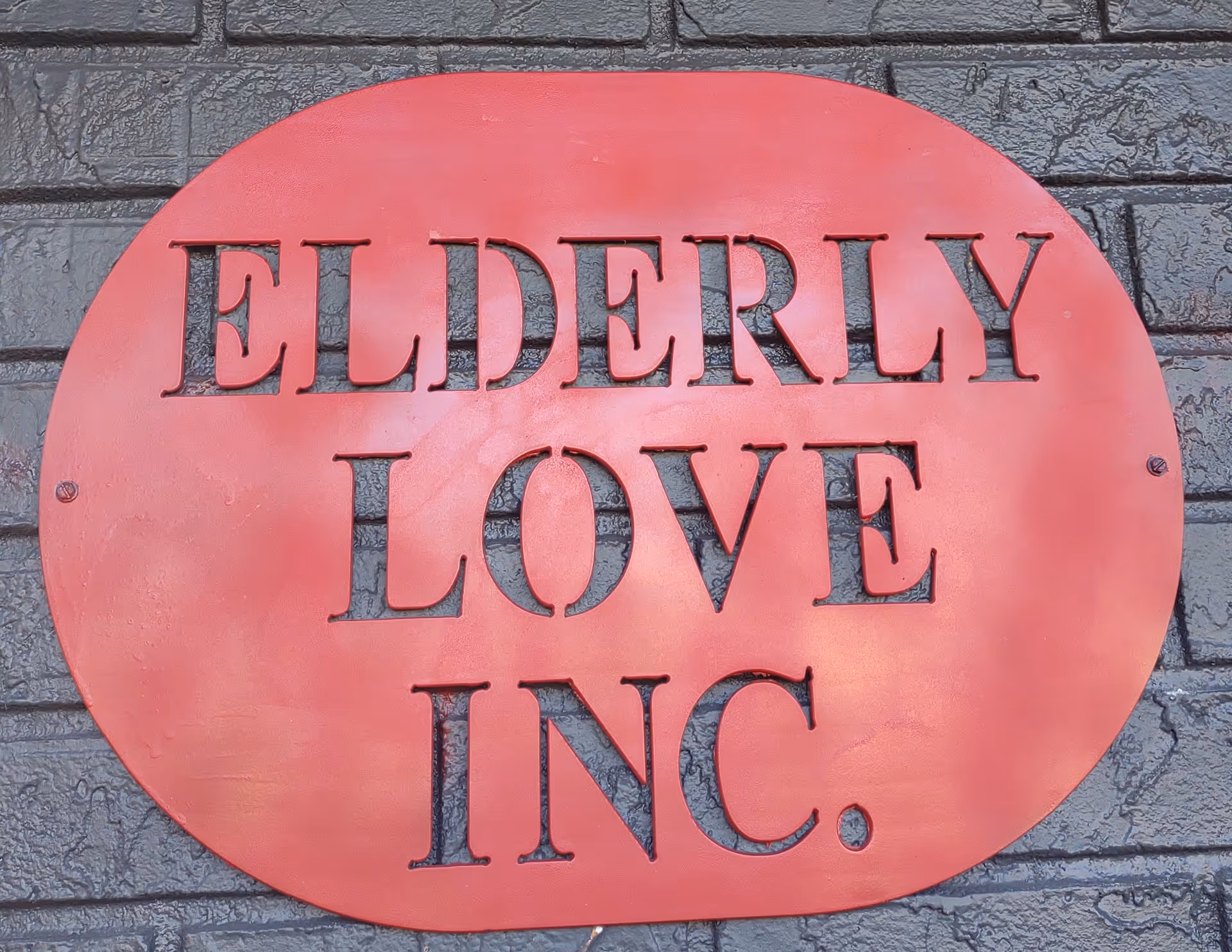 Red circular sign reading ELDERLY LOVE INC. mounted on a brick wall.