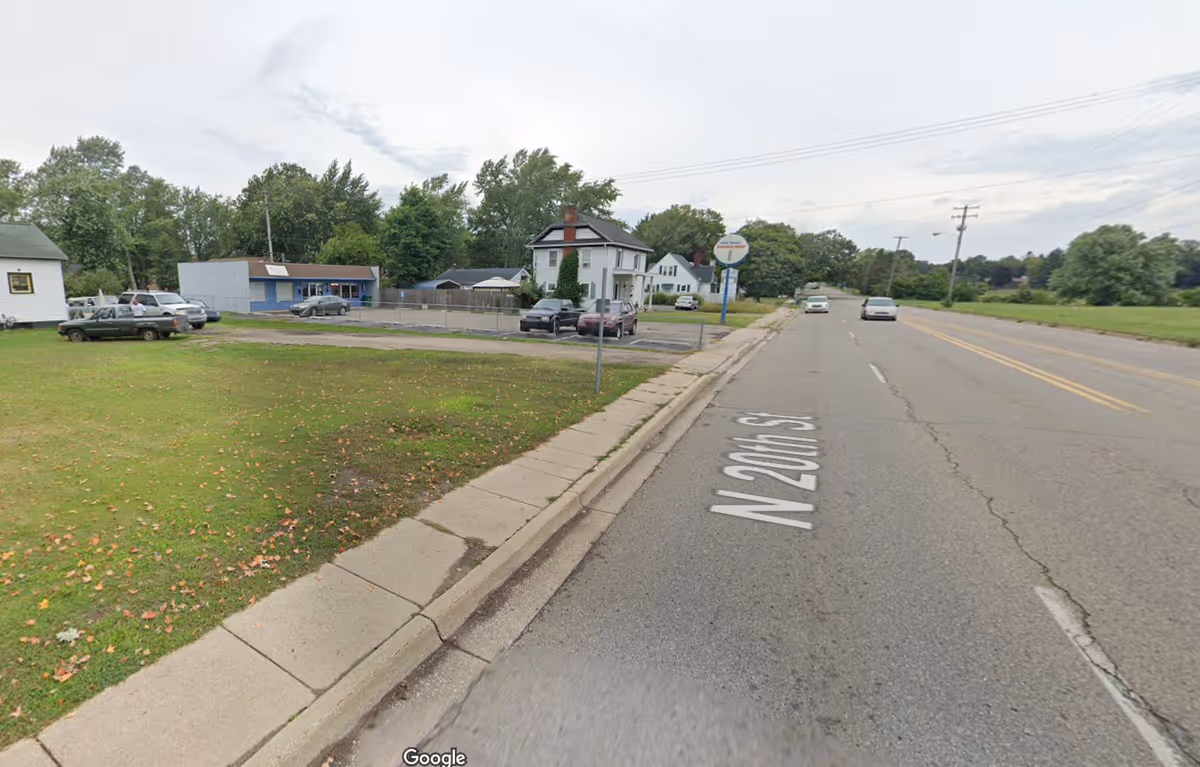 Street view of a small facility with a parking lot and grassy area beside a sidewalk.
