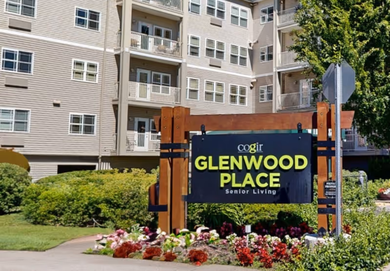 A landscaped entrance sign reading "Cogir GLENWOOD PLACE Senior Living" in front of a multi-story residential building.