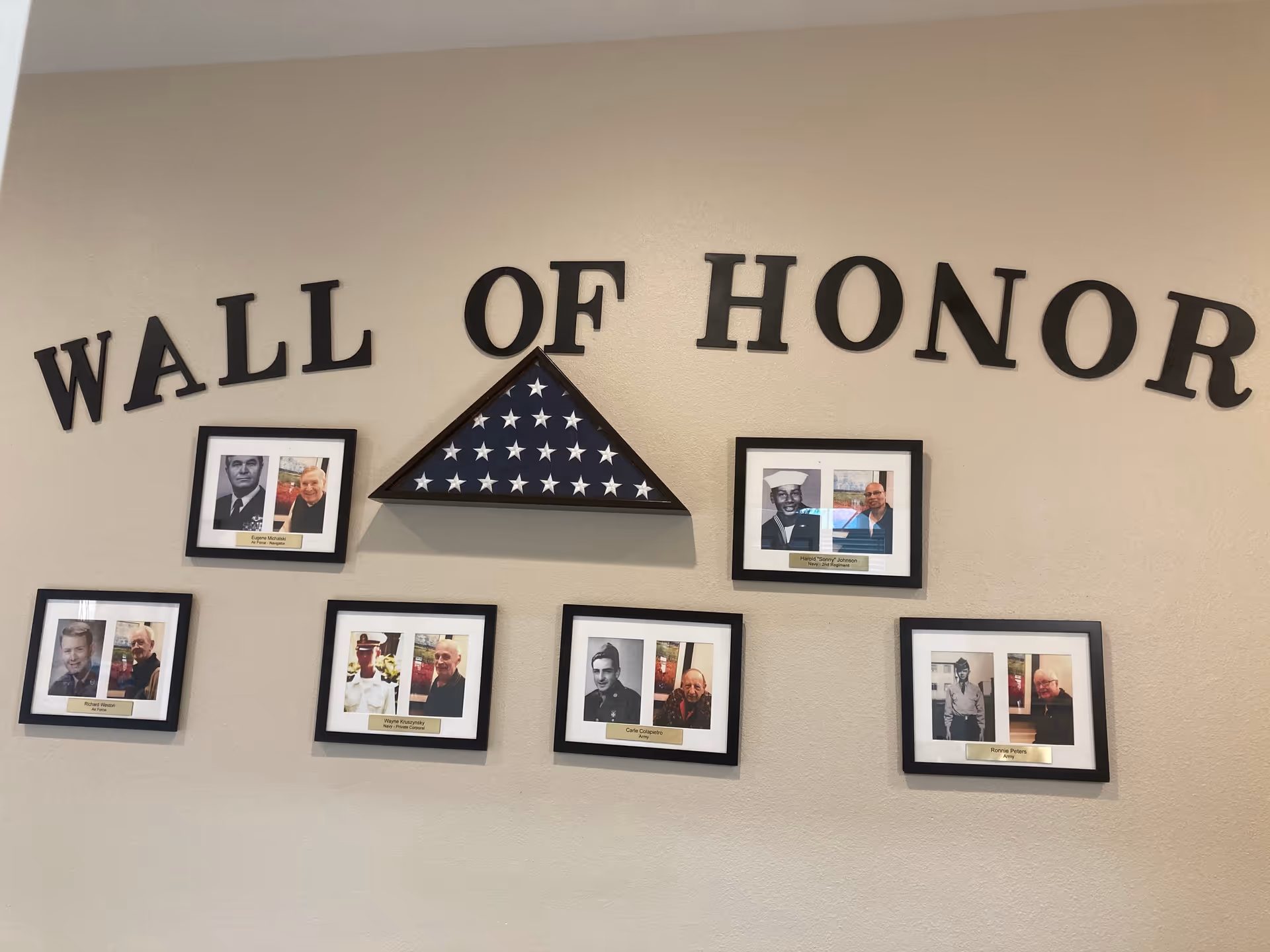 Interior wall display titled Wall of Honor with framed portraits and a folded flag.
