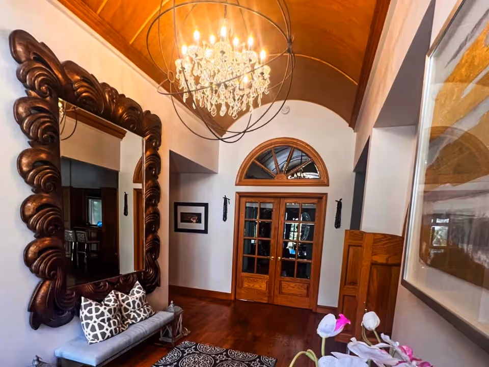 Elegant interior entry hall with a chandelier, ornate mirror, and wooden double doors.