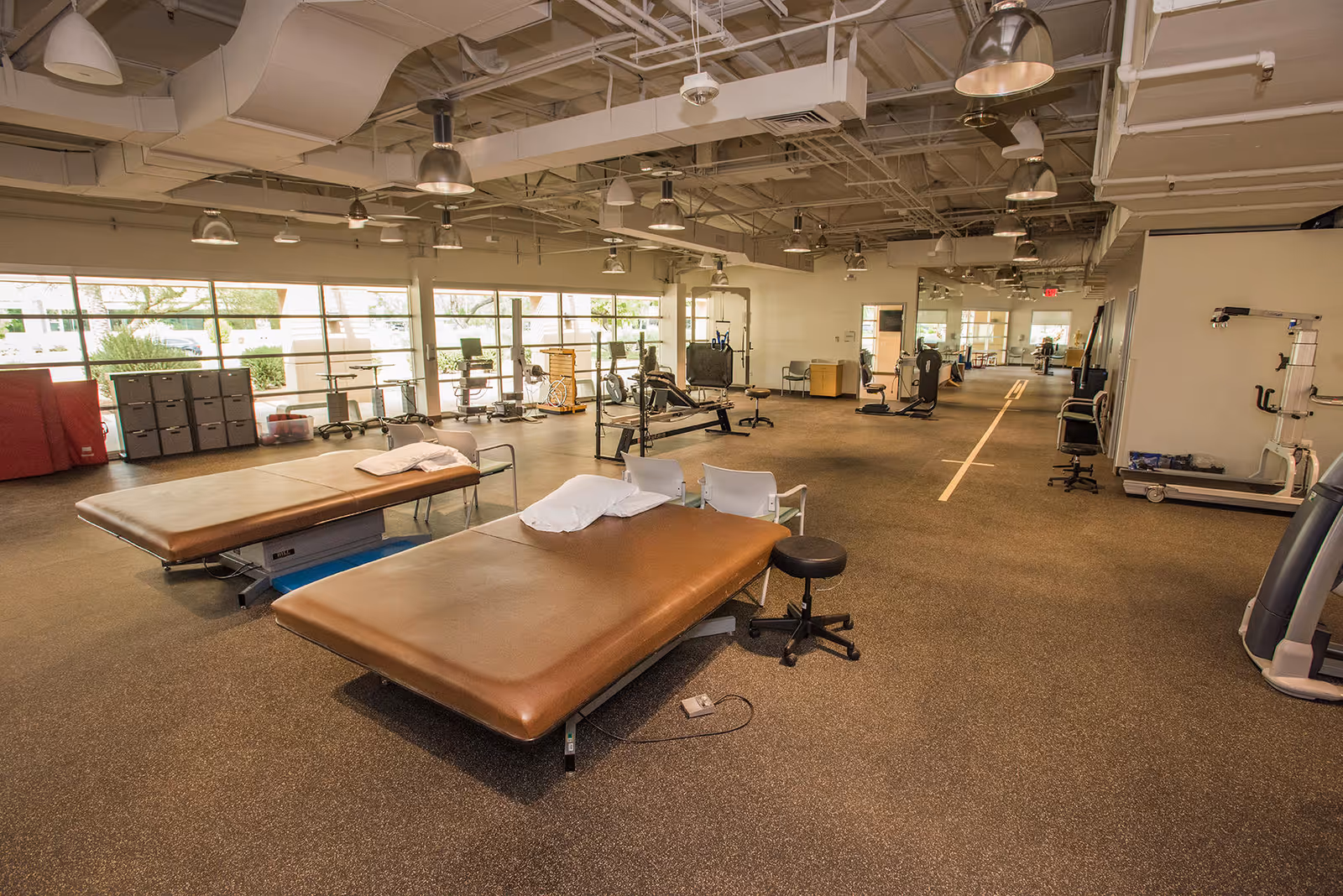 Open therapy gym featuring treatment tables, exercise equipment, and large windows.