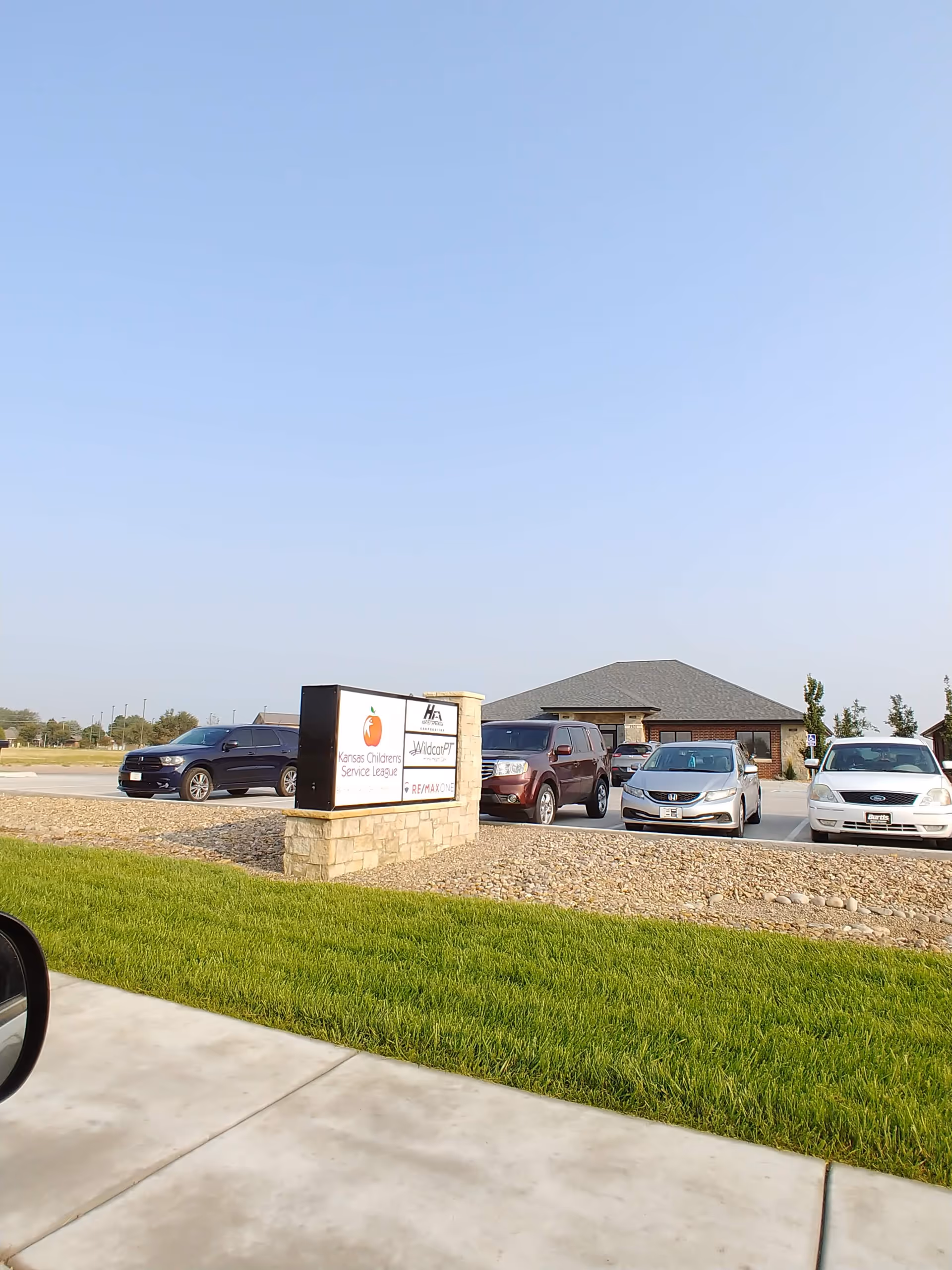 Exterior view of a facility with a stone sign and several parked cars.