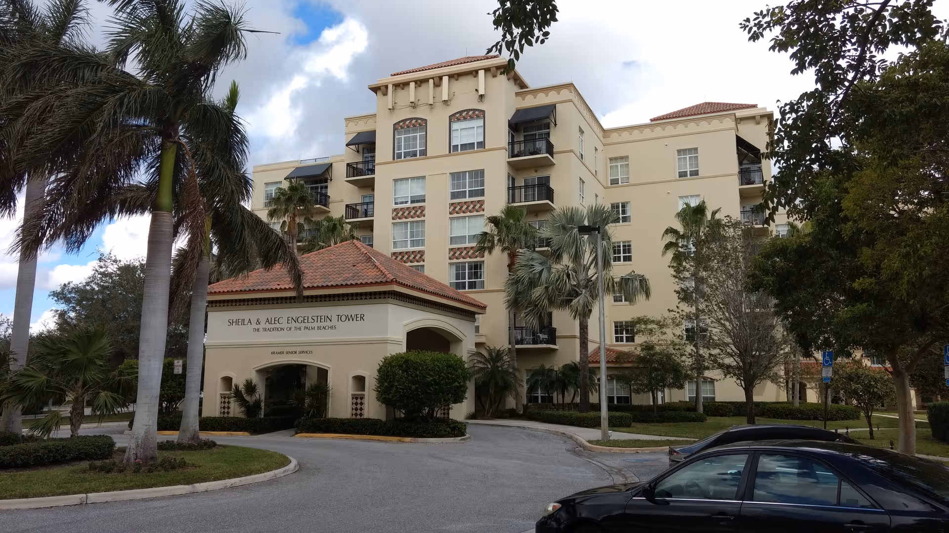 Exterior view of a beige senior living building with palm trees and a curved driveway.