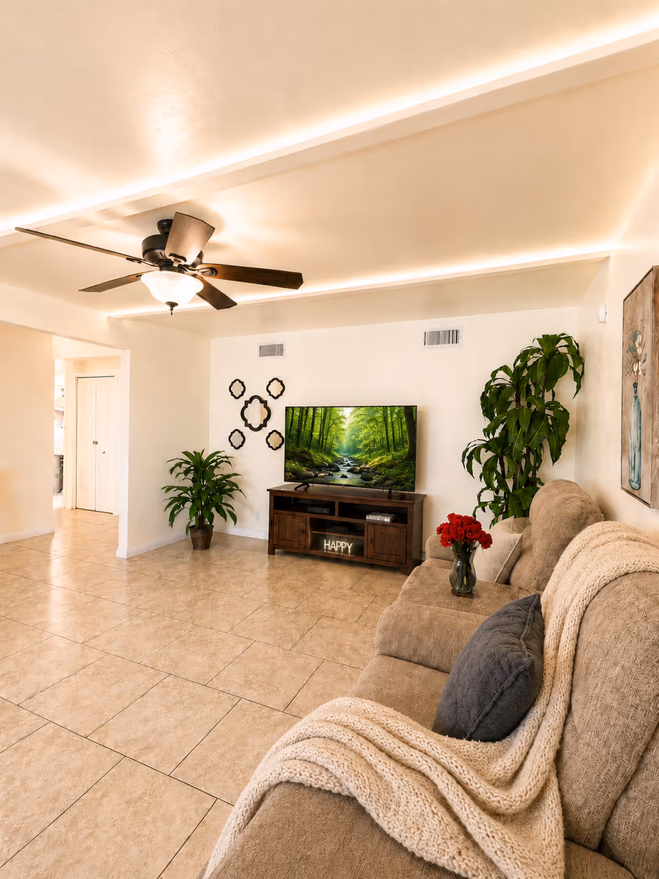 Bright living room with beige sofa, TV stand, plants, and a ceiling fan.