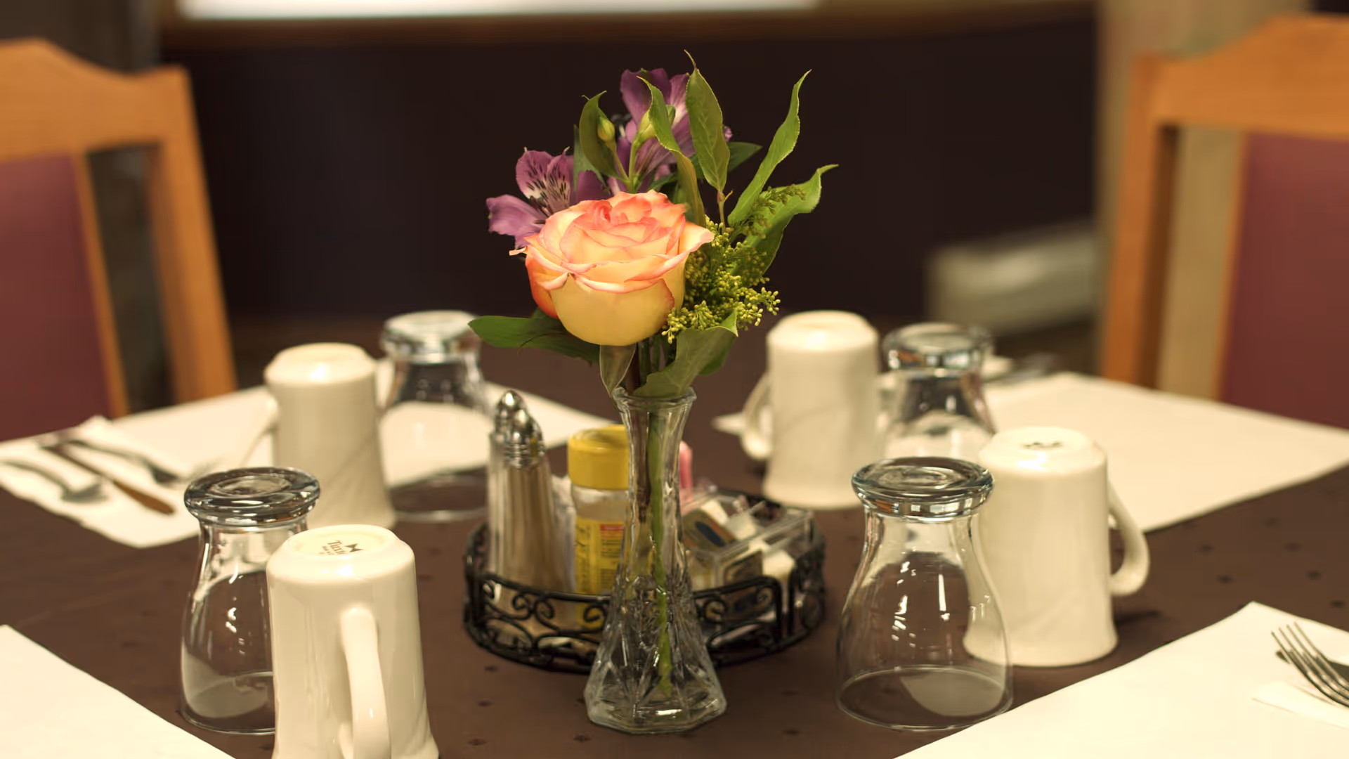A dining table set with a vase of flowers in a senior living facility dining room.