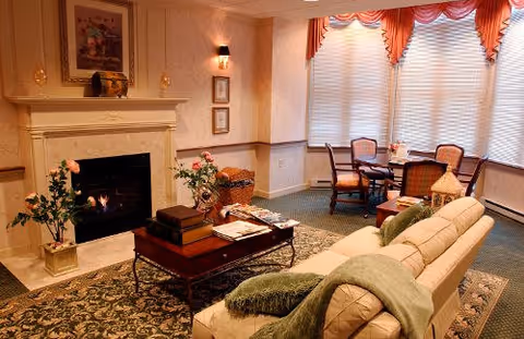 The Eastman House living room features a fireplace, sofa, chairs, and large window drapes.
