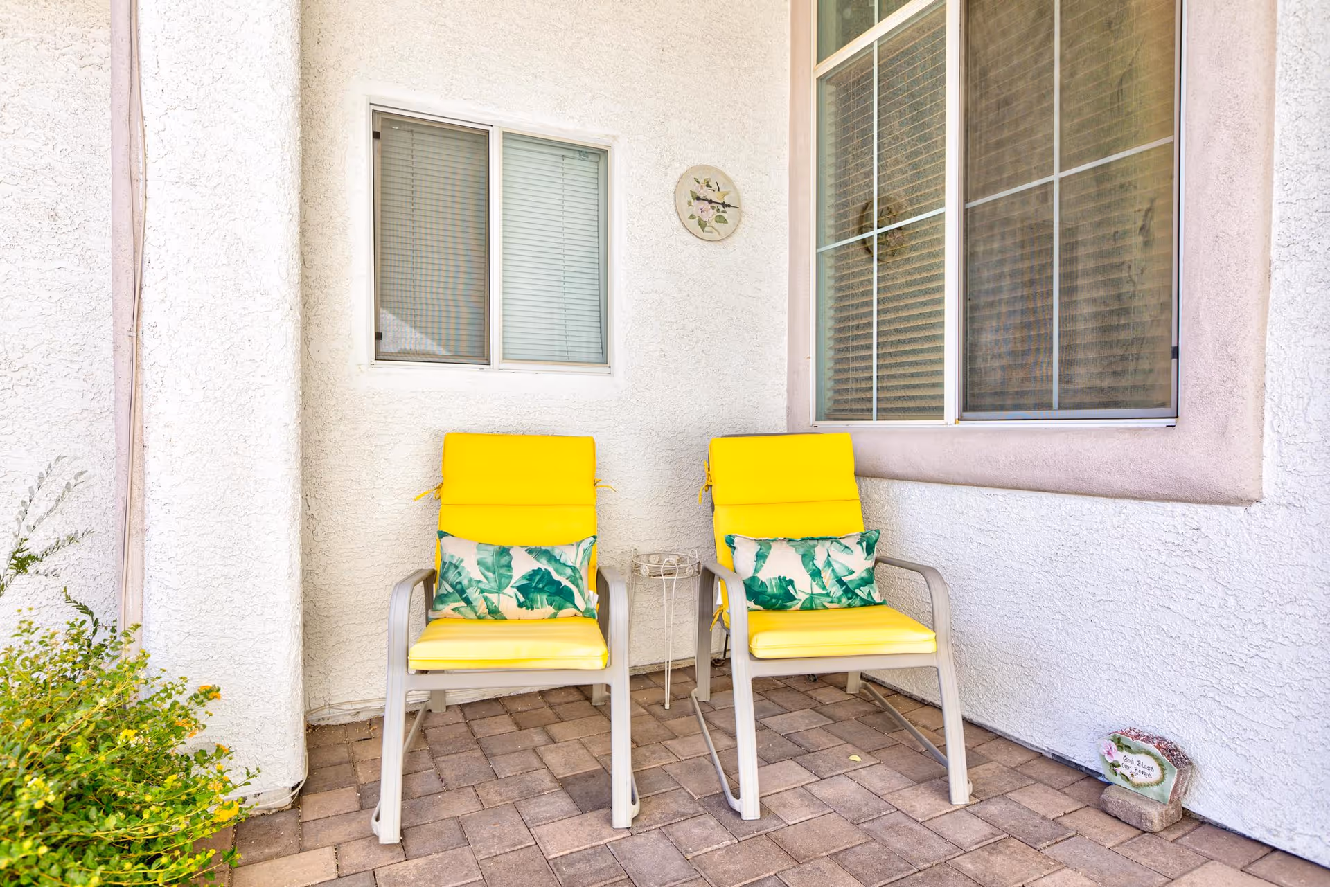 Two bright yellow patio chairs with tropical cushions sit on a brick outdoor patio.