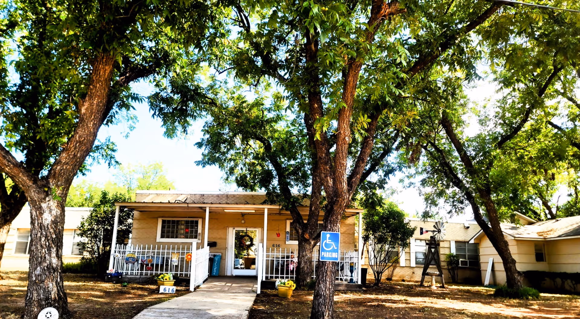 Single-story assisted living facility exterior with a covered entrance and large trees.