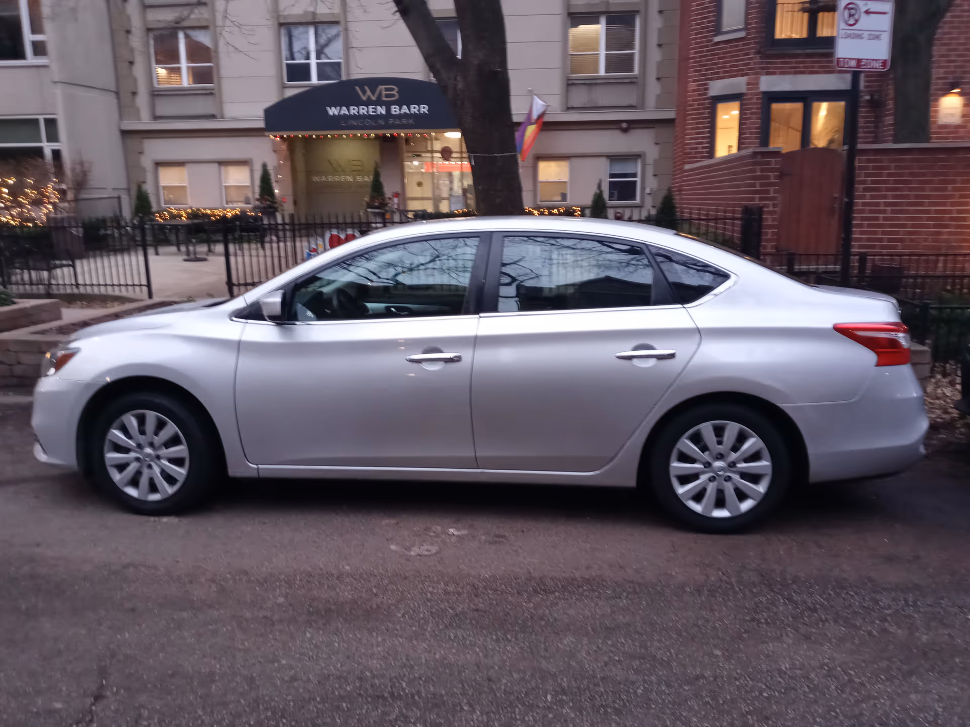 Silver sedan parked along a city street with Warren Barr Lincoln Park visible in background.