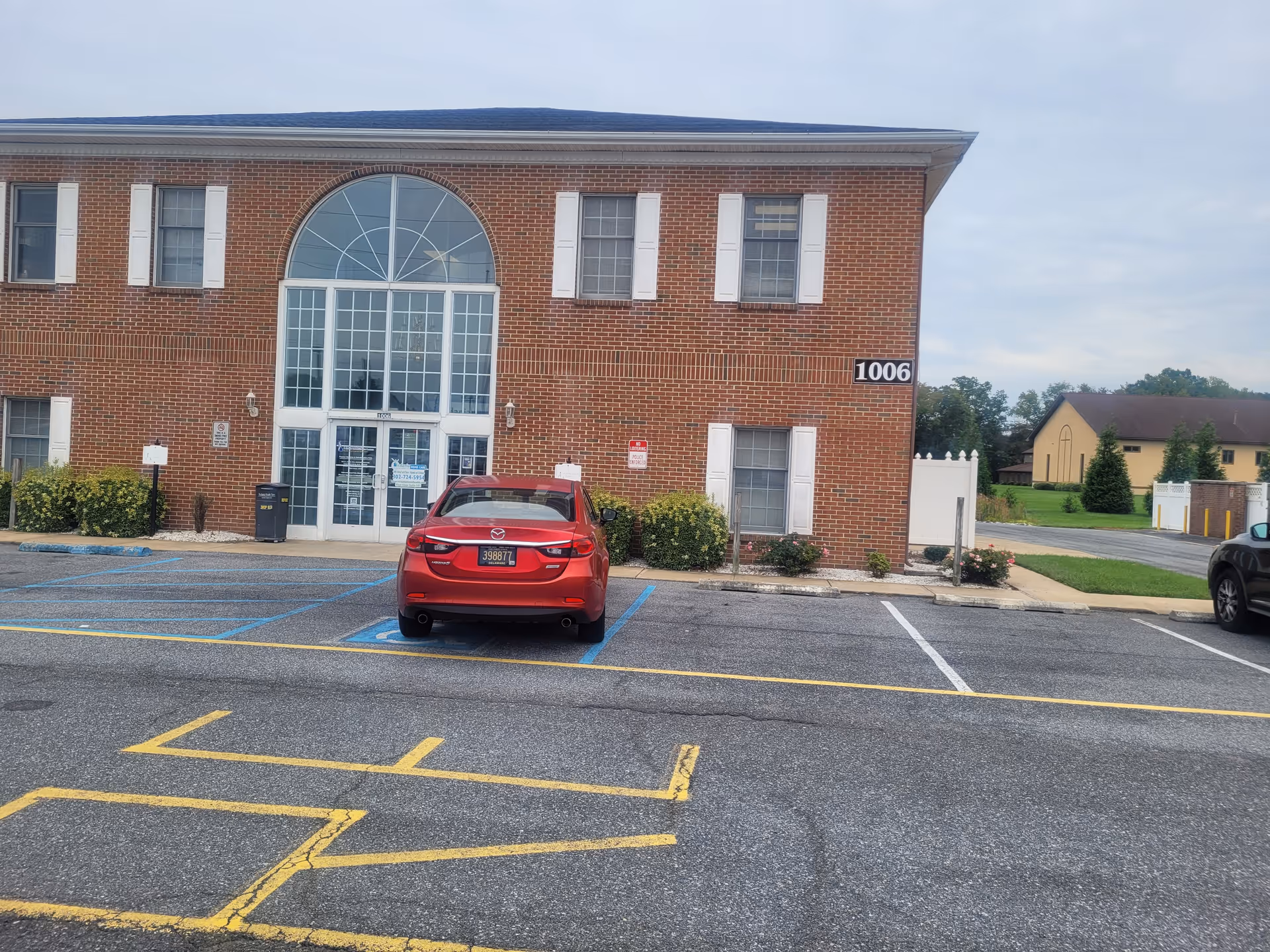 Red car parked in a lot in front of a brick senior living facility entrance.