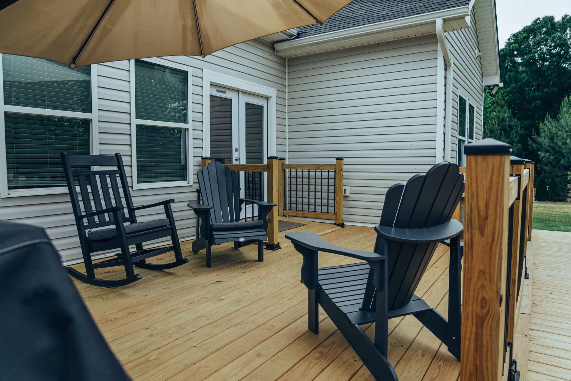 Outdoor wooden deck with chairs and an umbrella beside a light siding house