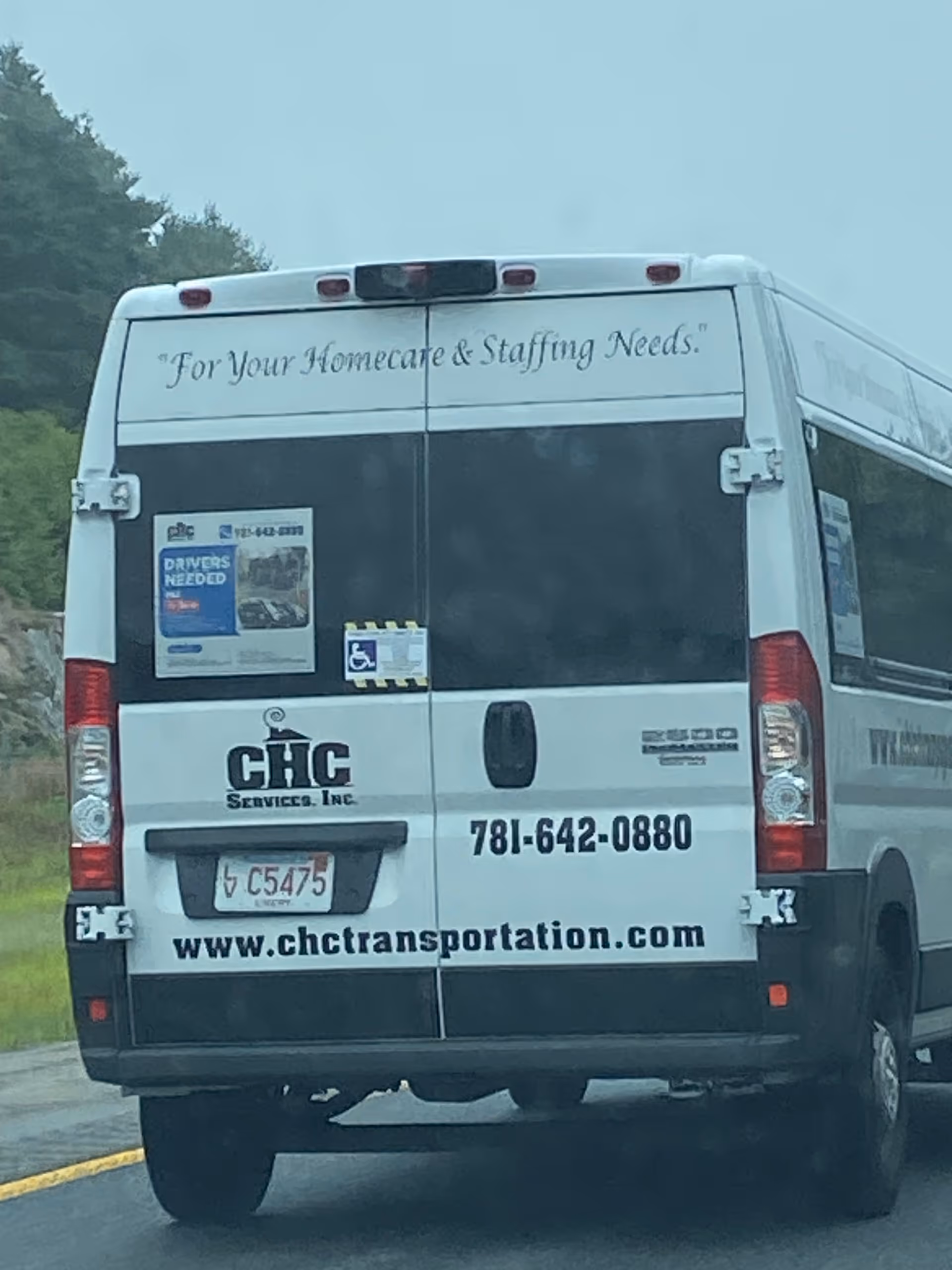 Rear view of a white CHC Transportation van on a roadway.