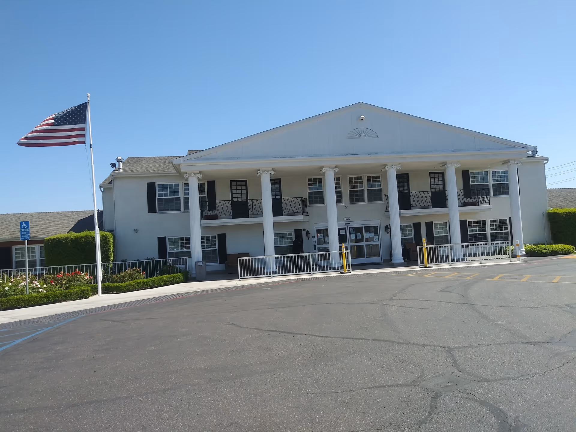Exterior view of a white, columned senior living facility with a flag at the entrance.