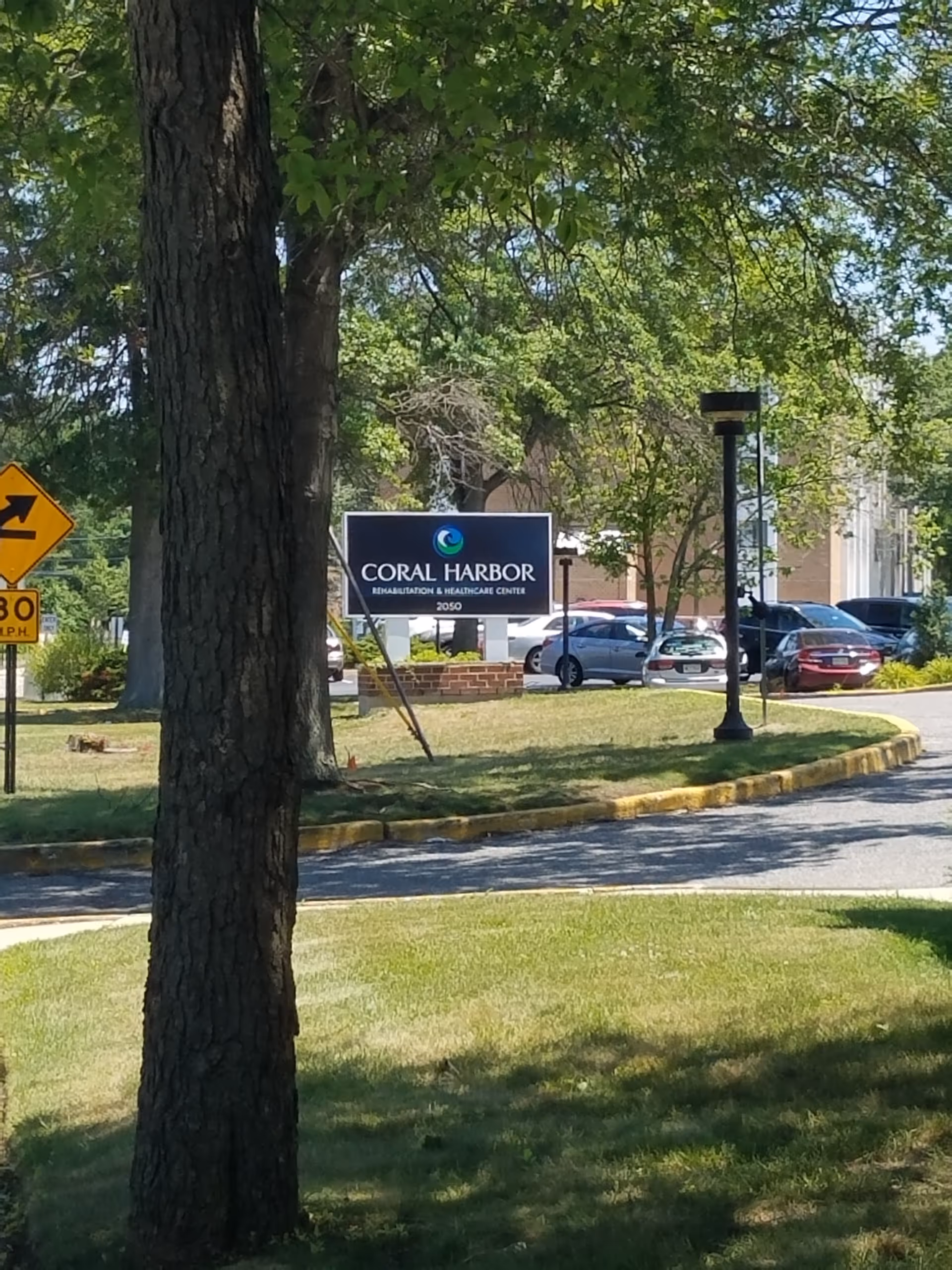 Outdoor view of Coral Harbor Rehabilitation and Healthcare Center sign by a parking lot.