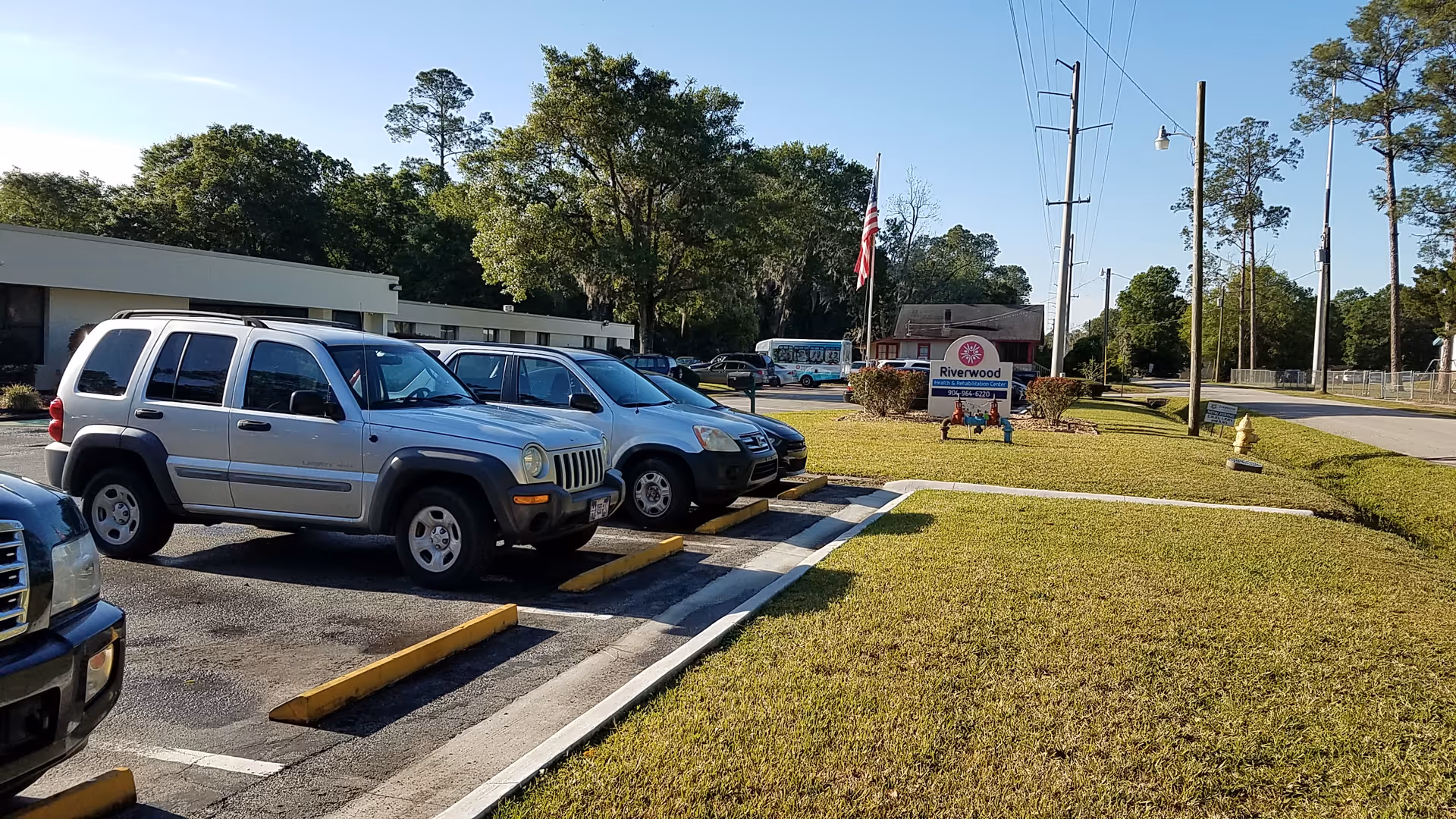 Parking lot in front of Riverwood Health & Rehabilitation Center with vehicles and trees.