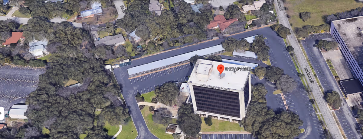 Aerial view of Therapy 2000 building with parking lot and surrounding trees.