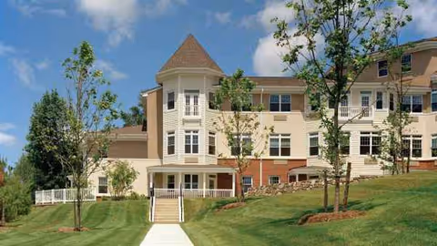 Atria Woodlands exterior features a turreted building, walkway, and manicured lawn.