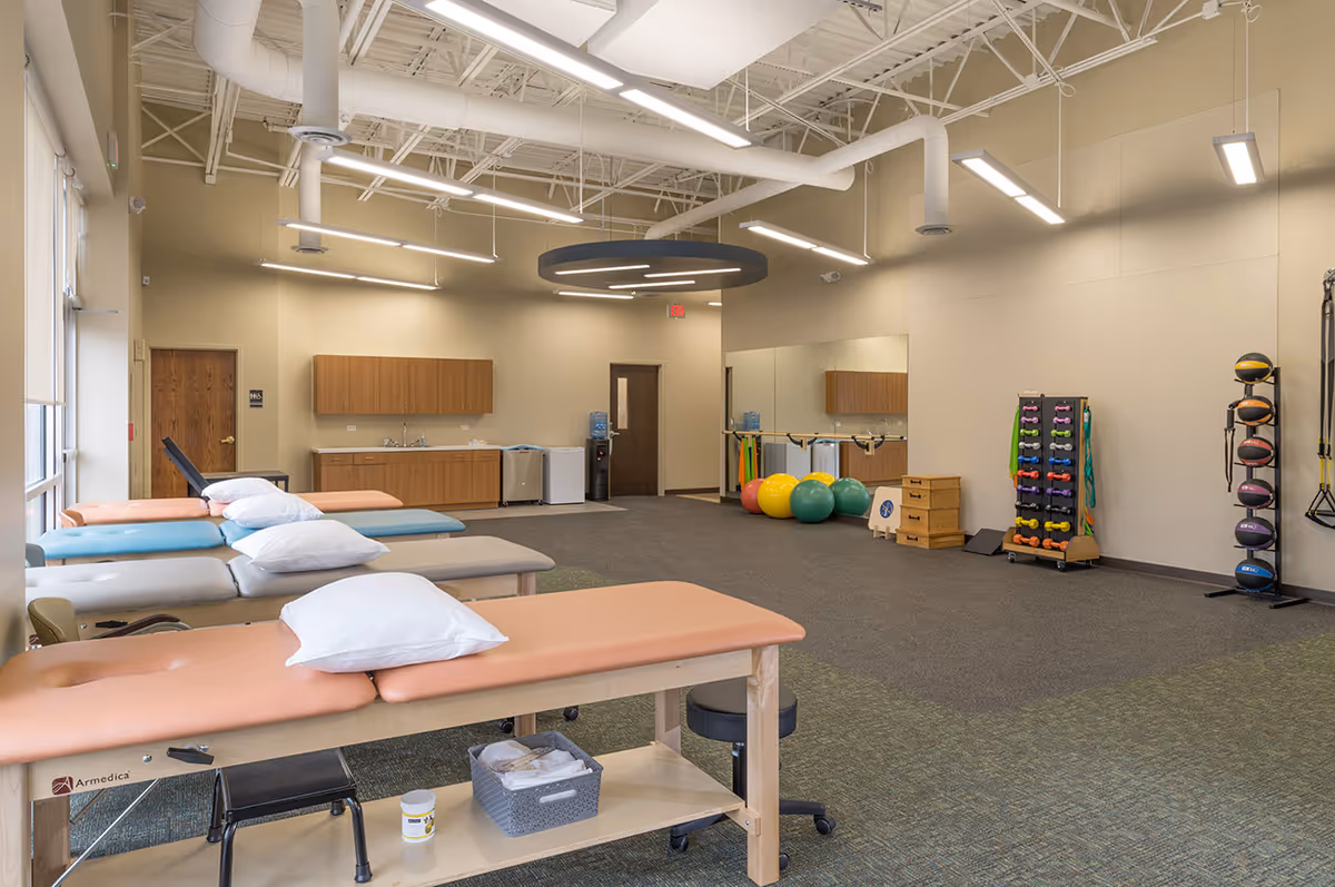 Interior of a physical therapy room with treatment tables, exercise equipment, and mirrors.