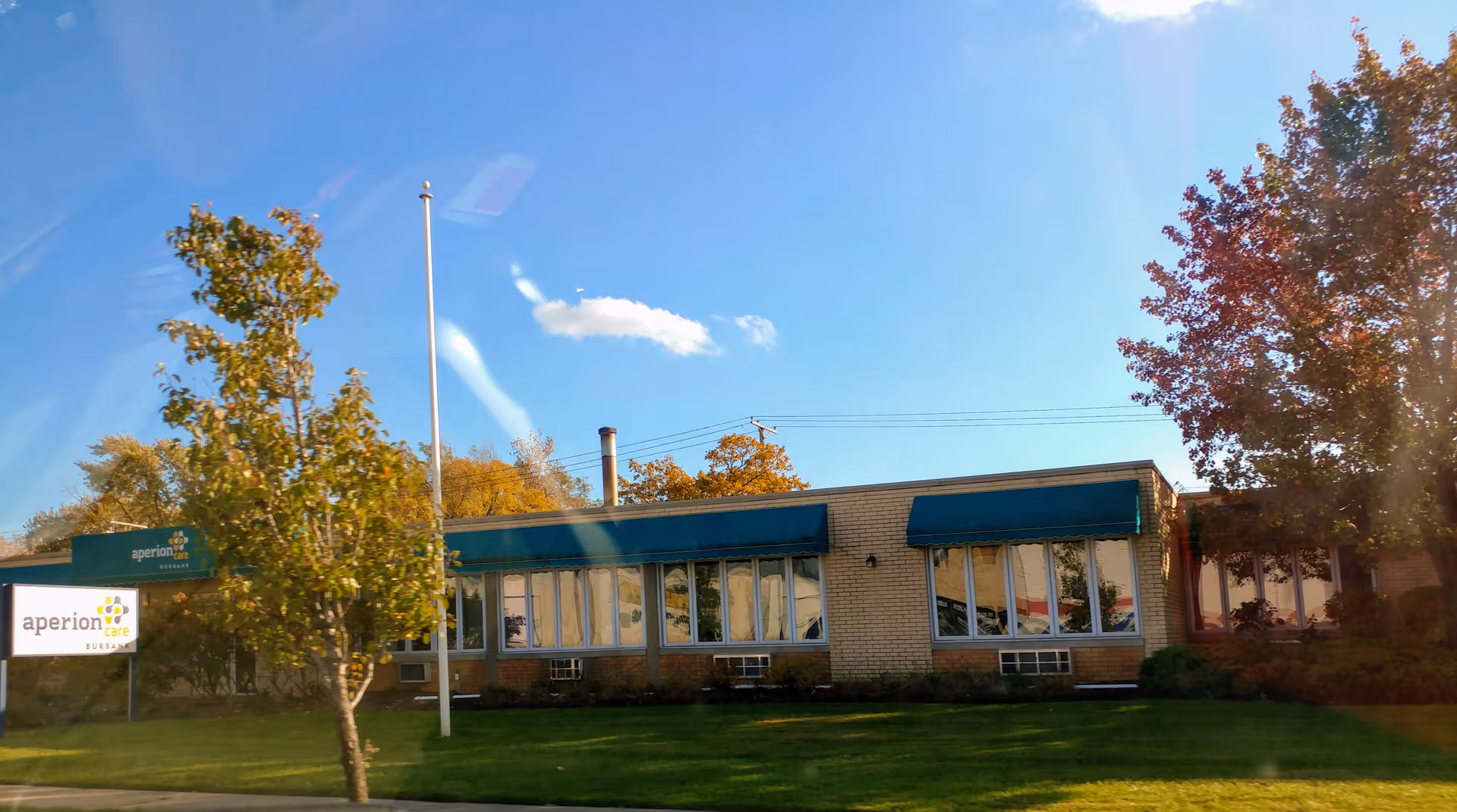 Single-story care facility with teal awnings and large windows along a green lawn.