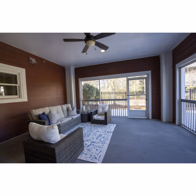Covered outdoor porch with wicker seating, rug, ceiling fan, and glass doors opening to yard.
