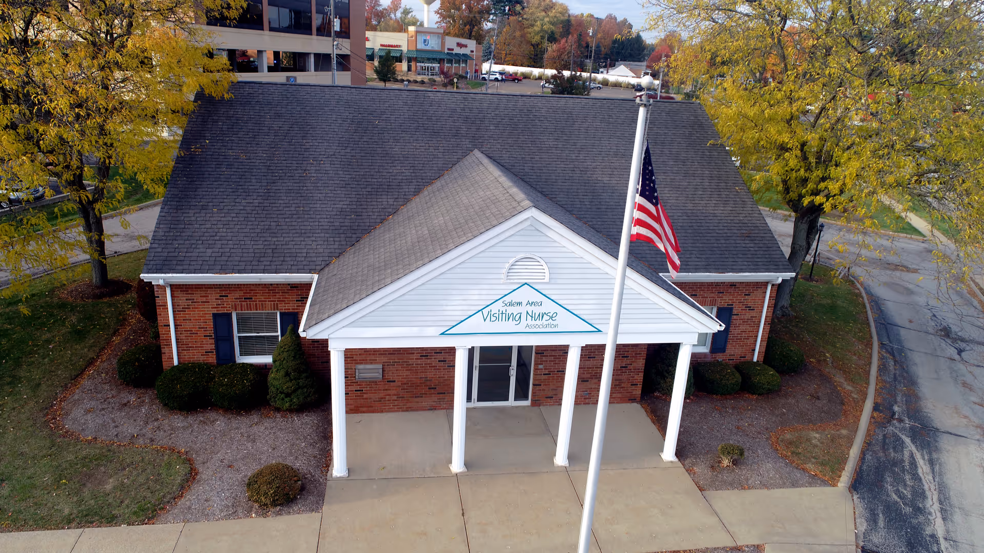 A brick building with a white portico, sign, and American flag outside.
