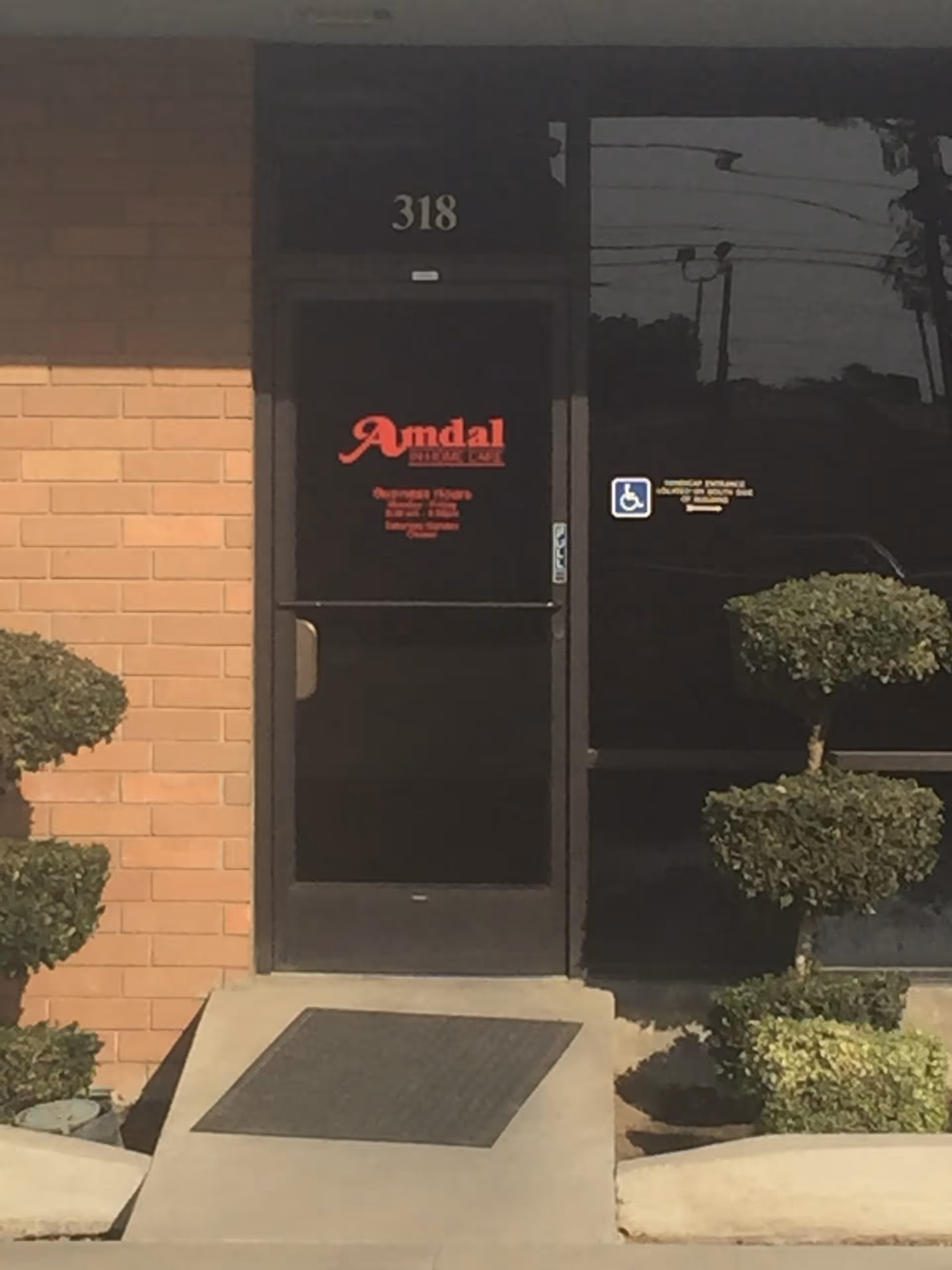 Entrance door of Amdal In-Home Care with brick exterior and pruned shrubs.