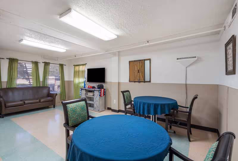 Common lounge area with round tables, blue tablecloths, green curtains, and a sofa.