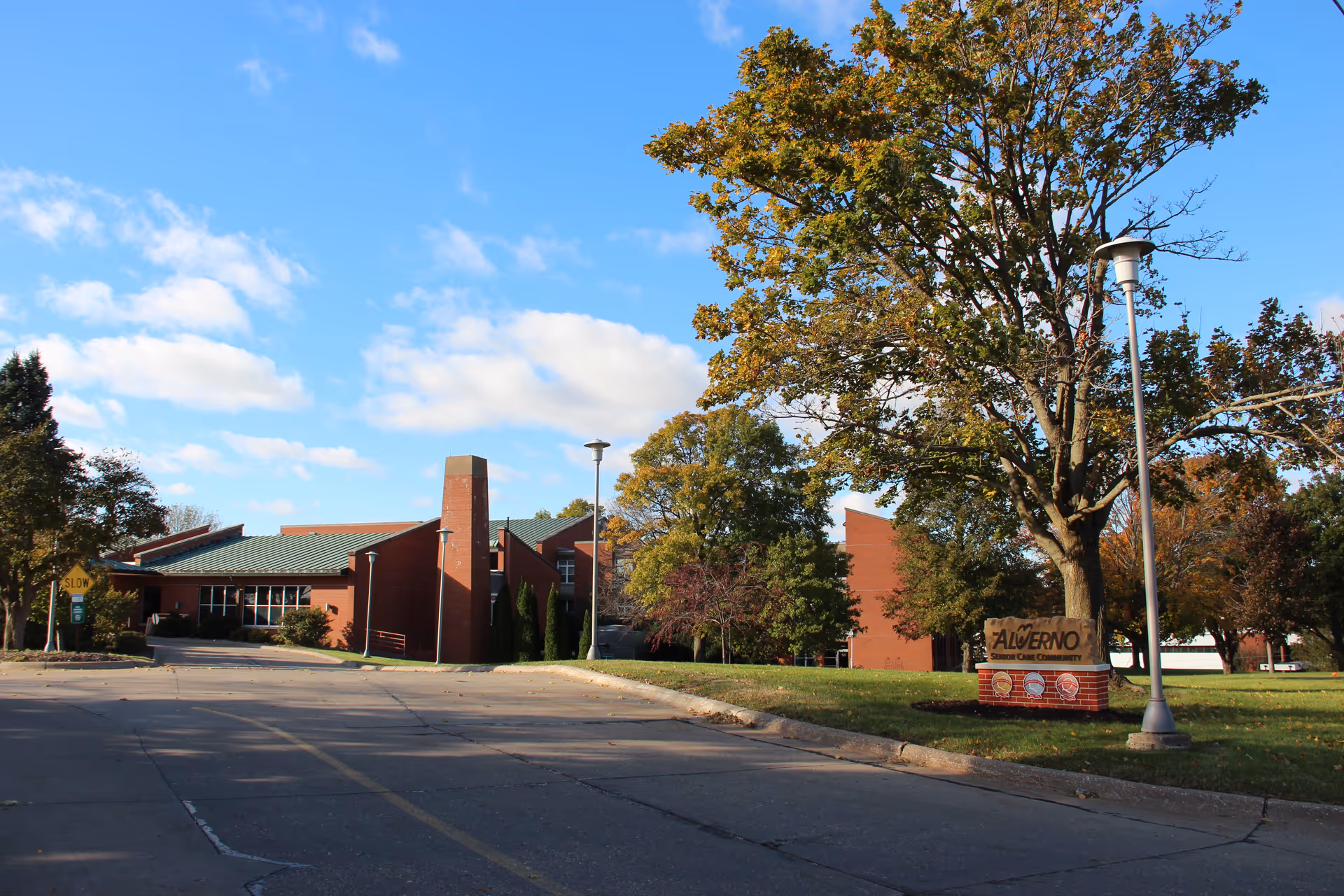 Front exterior view of The Alverno Senior Care Community with brick building, trees, and parking lot.