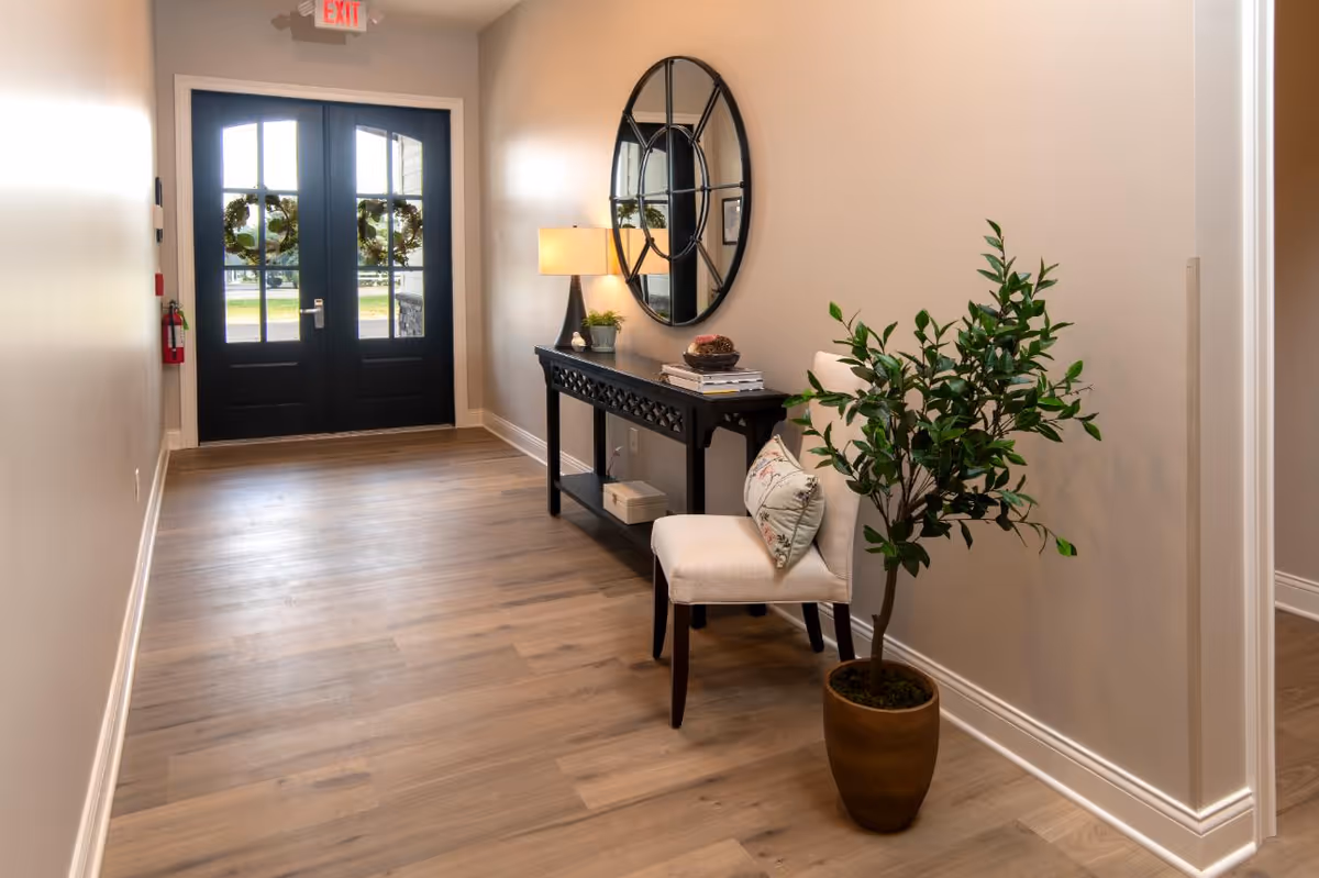 Interior hallway with console table, round mirror, lamp, chair, and potted plant.